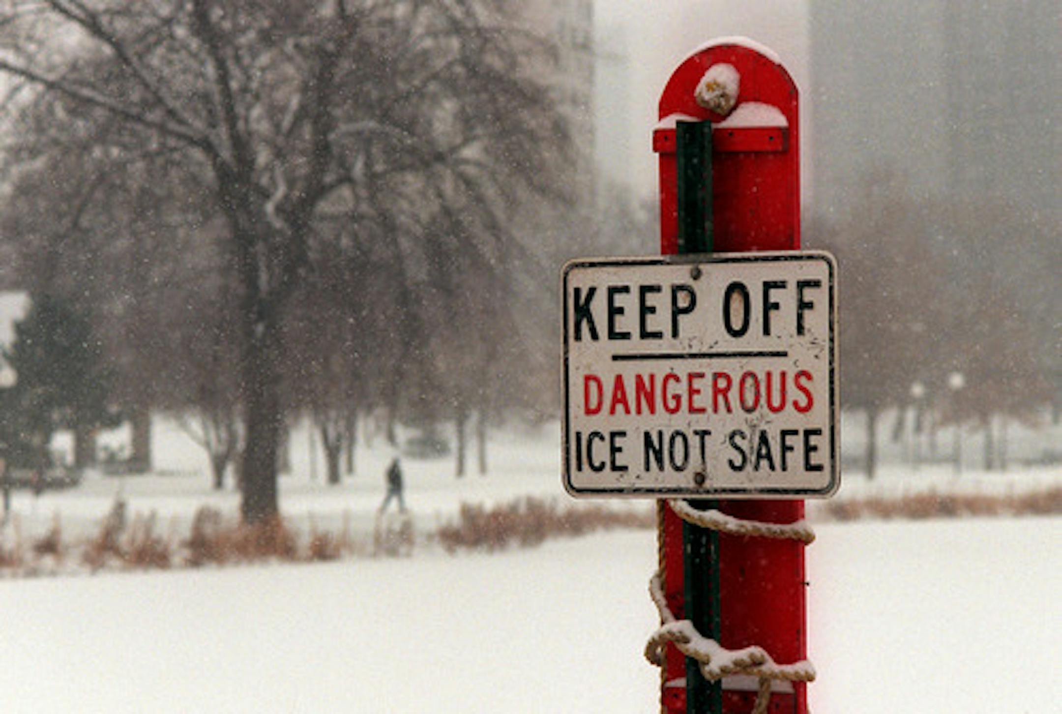 Minneapolis,MN Thursday 12/23/99 Unsafe ice conditions in the metro area -- This sign a Loring pond in Minneapolis reads KEEP OFF - DANGEROUS-ICE NOT SAFE. The pond is in the near foreground and the pedestrian in the background is walking along a path in Loring Park