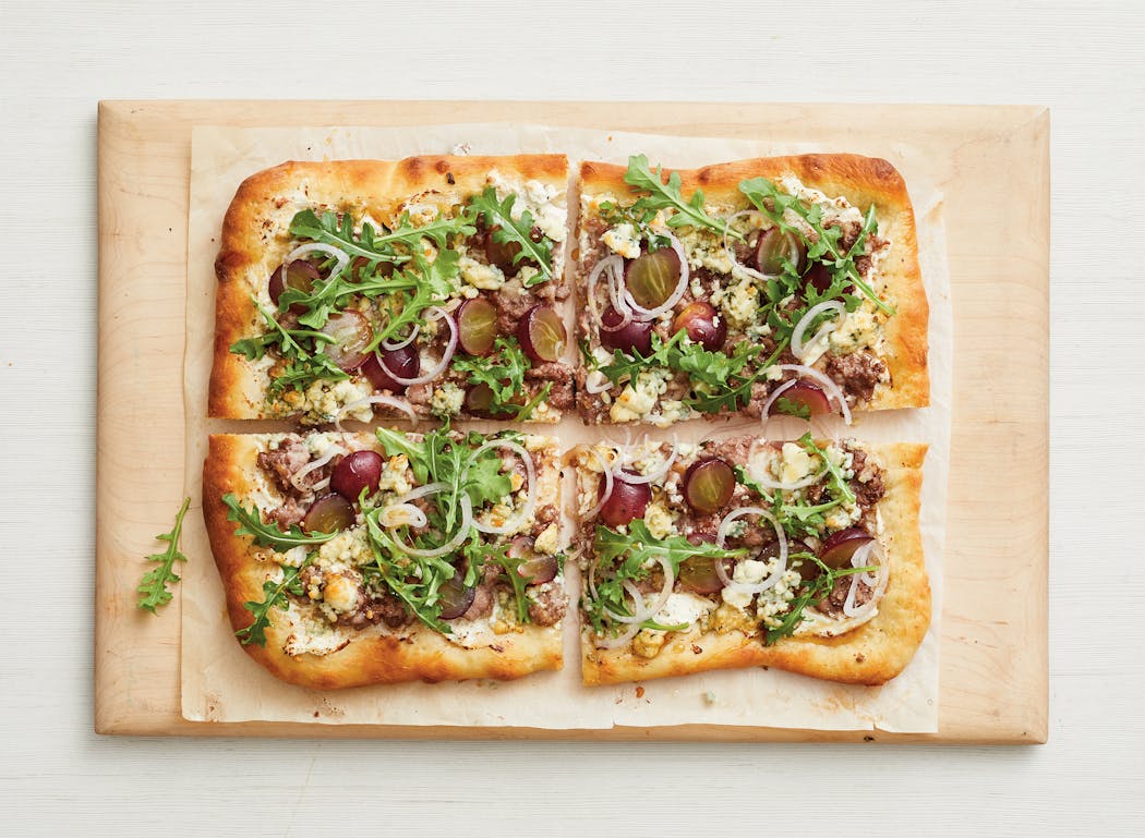 Sausage, arugula and grapes top this rectangle pizza. From the Food Network’s “The Big Book of Pizza.”