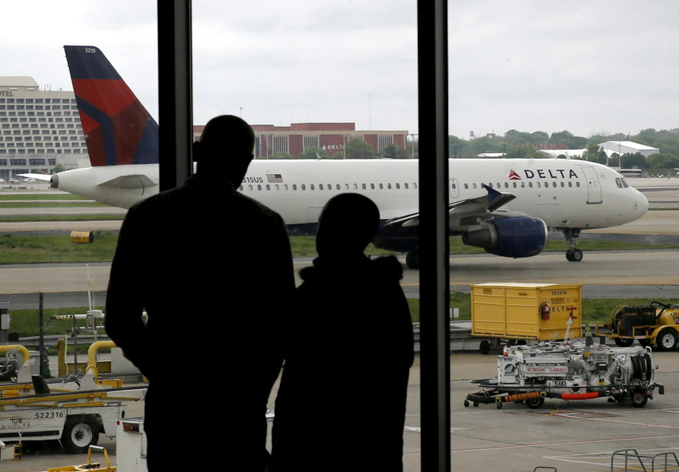 In this Tuesday, April 14, 2015 photo, travelers watch as a plane taxis at Hartsfield-Jackson Atlanta International Airport in Atlanta. After years of steadily-rising airfare, travelers this summer can expect a tiny bit of relief, a really tiny bit. The average roundtrip domestic ticket this summer now stands at $454, down $2.01 from last summer. Vacationers to Europe will fare better with tickets down 3 percent to $1,619, about $50 less. (AP Photo/Charles Rex Arbogast)