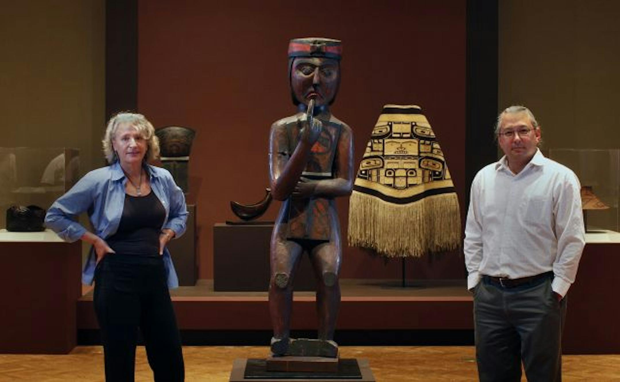Curators Eva Fognell and Joe Horsecapture posed with a painted figure of a Kwakiutl chief, carved from cedar and painted in the late 1800s on Vancouver Island.
