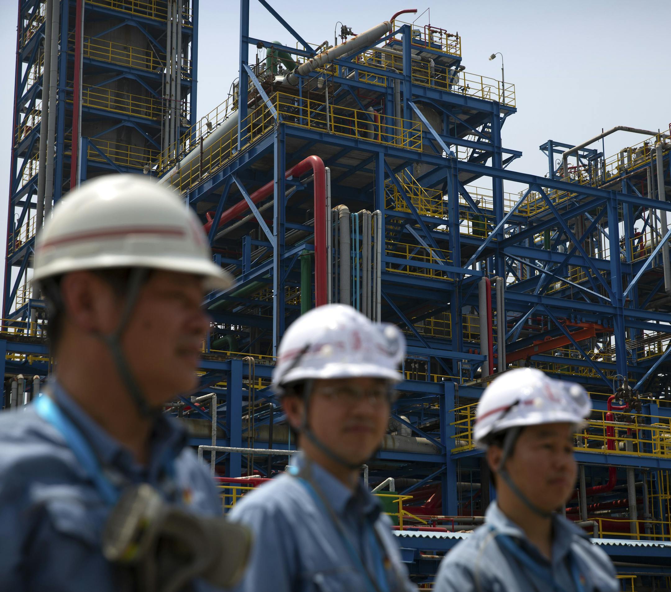 FILE - In this May 25, 2018, file photo, workers stand near facilities for producing polypropylene at the Sinopec Yanshan Petrochemical Company on the outskirts of Beijing. China's government promised Monday to open its oil, telecom and power markets wider to private competitors as the ruling Communist Party tries to shore up growth in the slowing, state-dominated economy. (AP Photo/Mark Schiefelbein, File)
