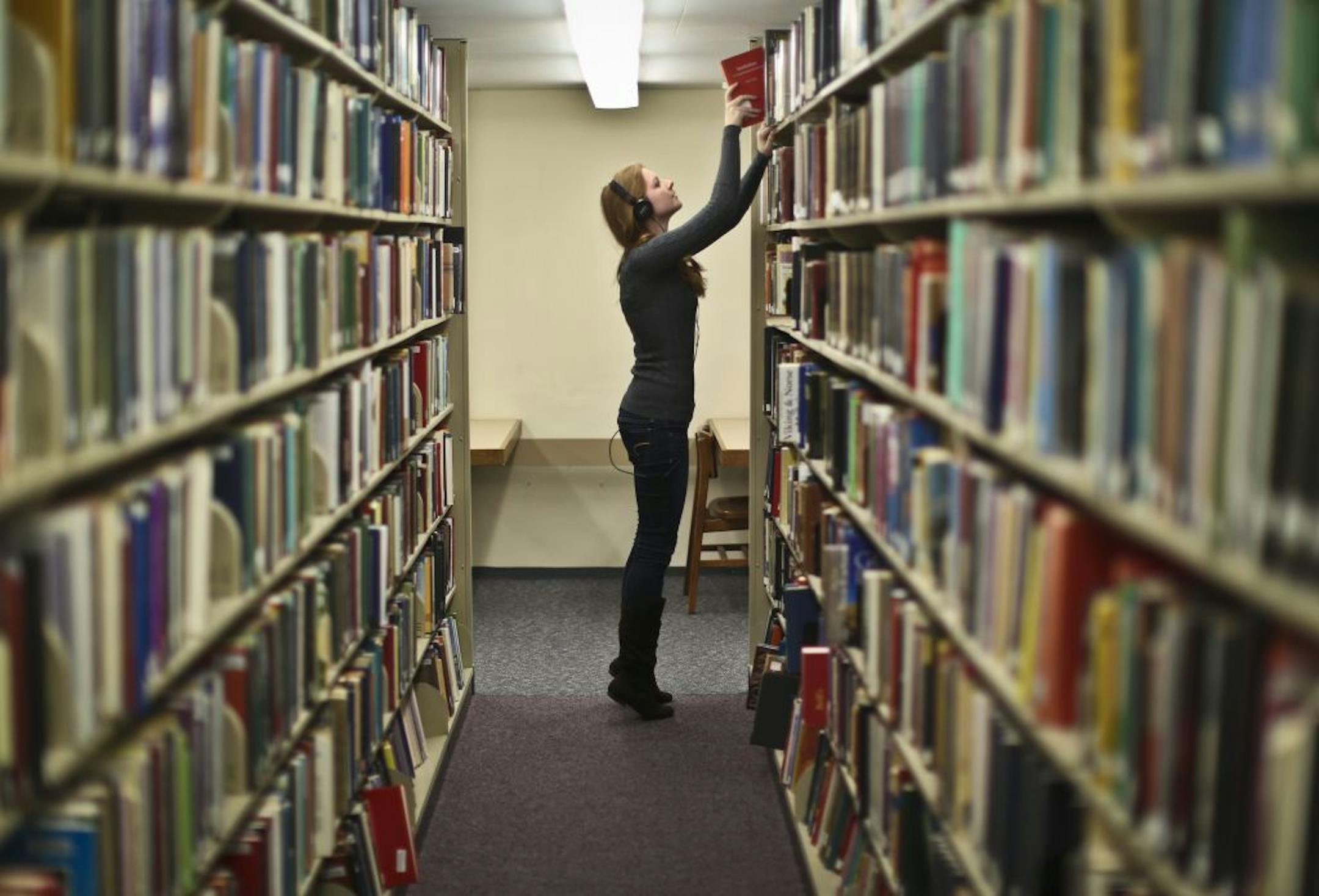 Library student worker Sam Botz returned books to the shelves at the library at St. Olaf College in Northfield, Minn., on Wednesday, December 5, 2012. The two private, nonprofit Northfield colleges are studying whether they'd save money by merging many back-office operations.
