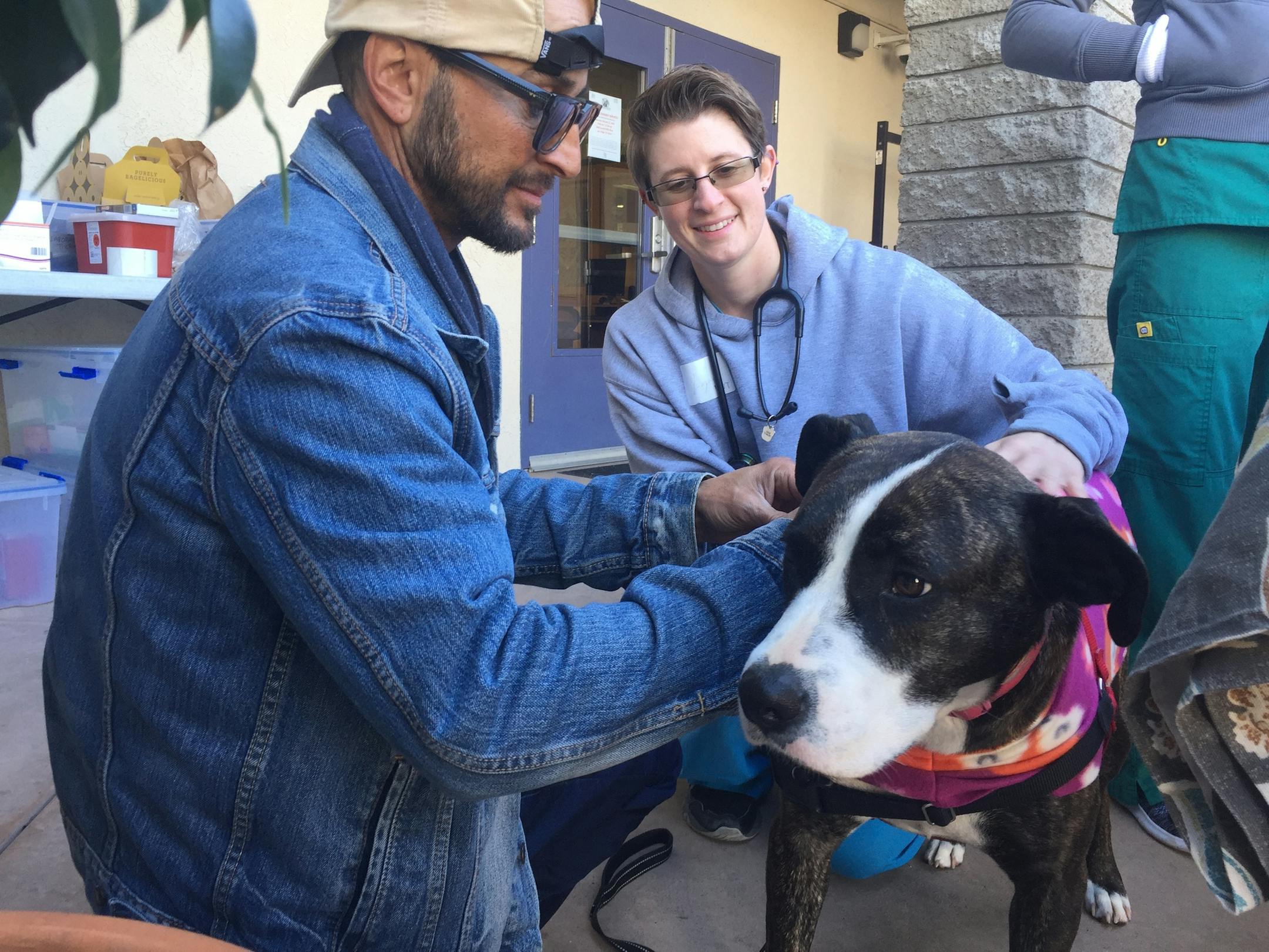 Michael Austin (left) and registered veterinarian technician Logan Gonella put a pet jacket on Austinâ€™s dog, Chloe, at a Street Dog Coalition clinic in Ocean Beach.(Gary Warth) (Gary Warth/San Diego Union-Tribune/TNS)