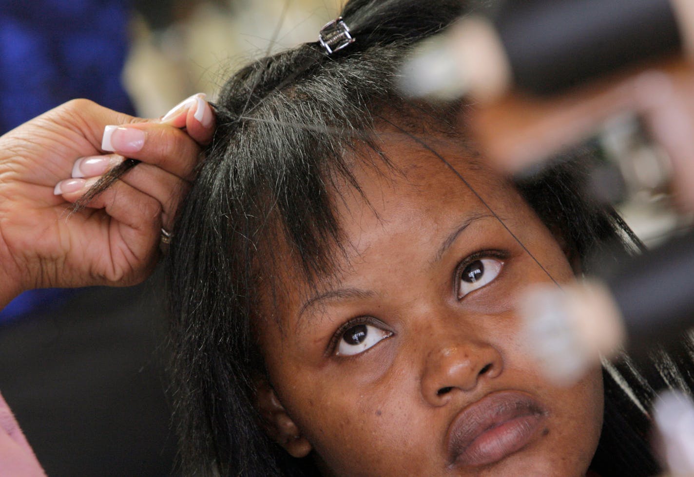 Nativia Humphrey looks up as salon owner Kimberly Givens uses three spools of wax covered polyester and cotton thread to weave a "weft" into her hair as she gets a Christina Method hair weaving at Soultry Scissors on Northfield Ave. The weft creates a line of real hair and thread that the extensions can be sewn on onto.