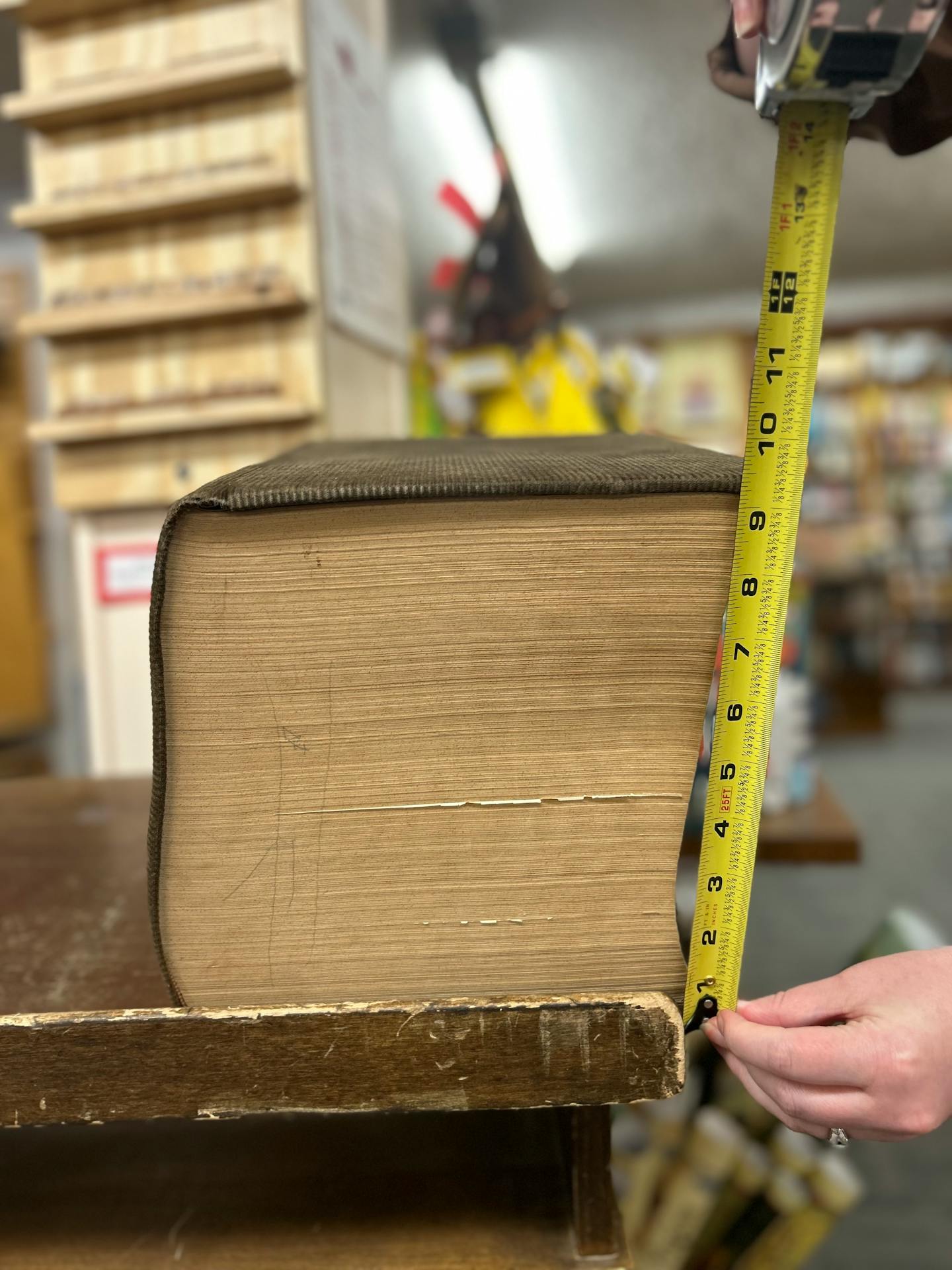 A corduroy bound dictionary weighing over 25 pounds and measuring 9 inches tall sits on a rickety wooden end table in a bookstore.