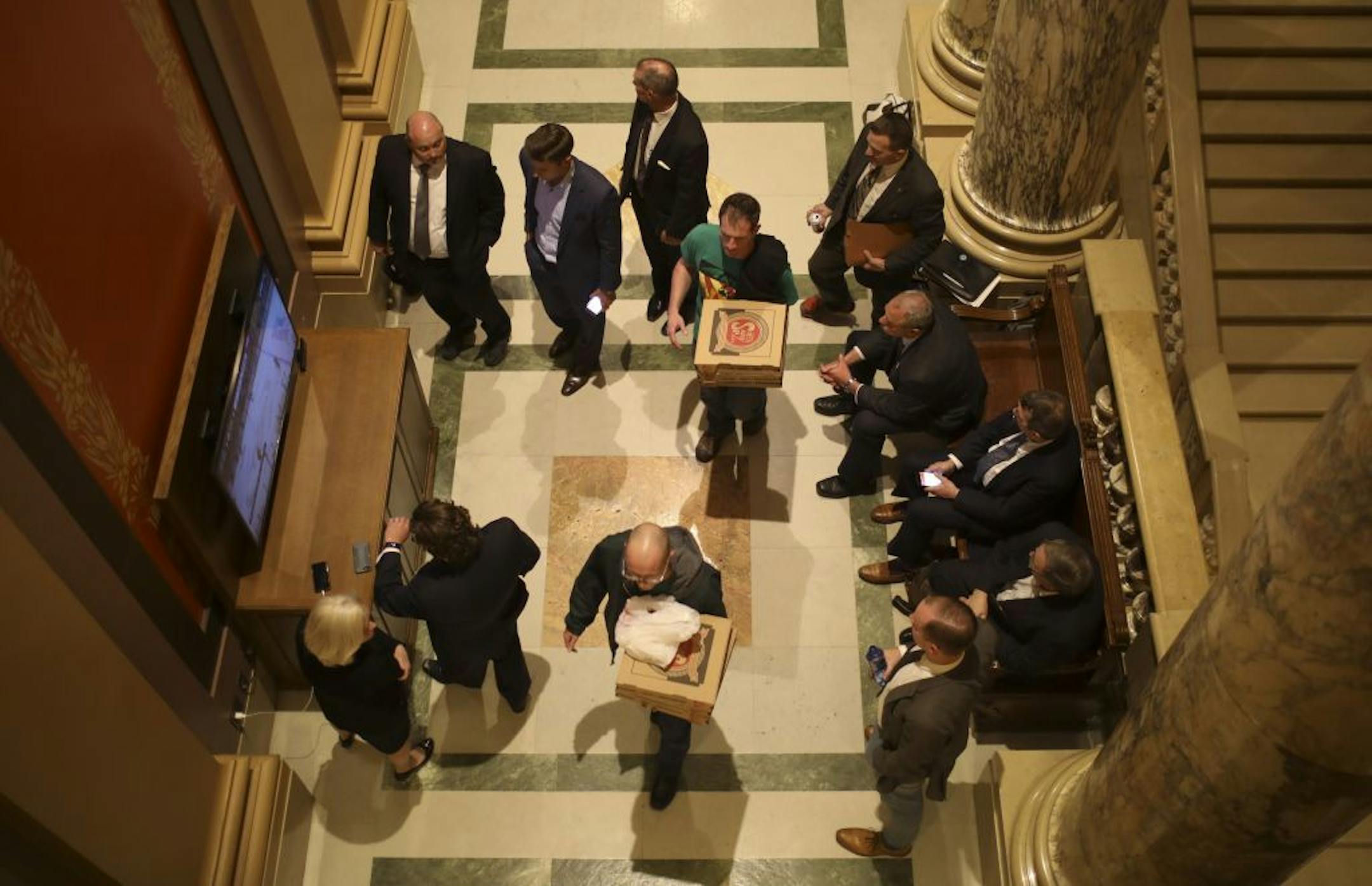 Pizzas delivery guys cut through a group watching an NHL playoff game on a television monitor in a hallway of the State Capitol Monday night with the House and Senate still in recess and the clock ticking.
