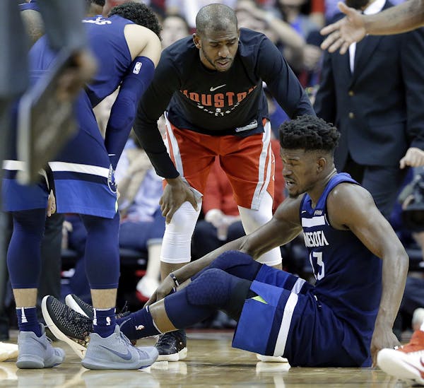 Minnesota Timberwolves guard Jimmy Butler (23) reacts to a knee injury on the court as Houston Rockets guard Chris Paul (3) hovers over him during the