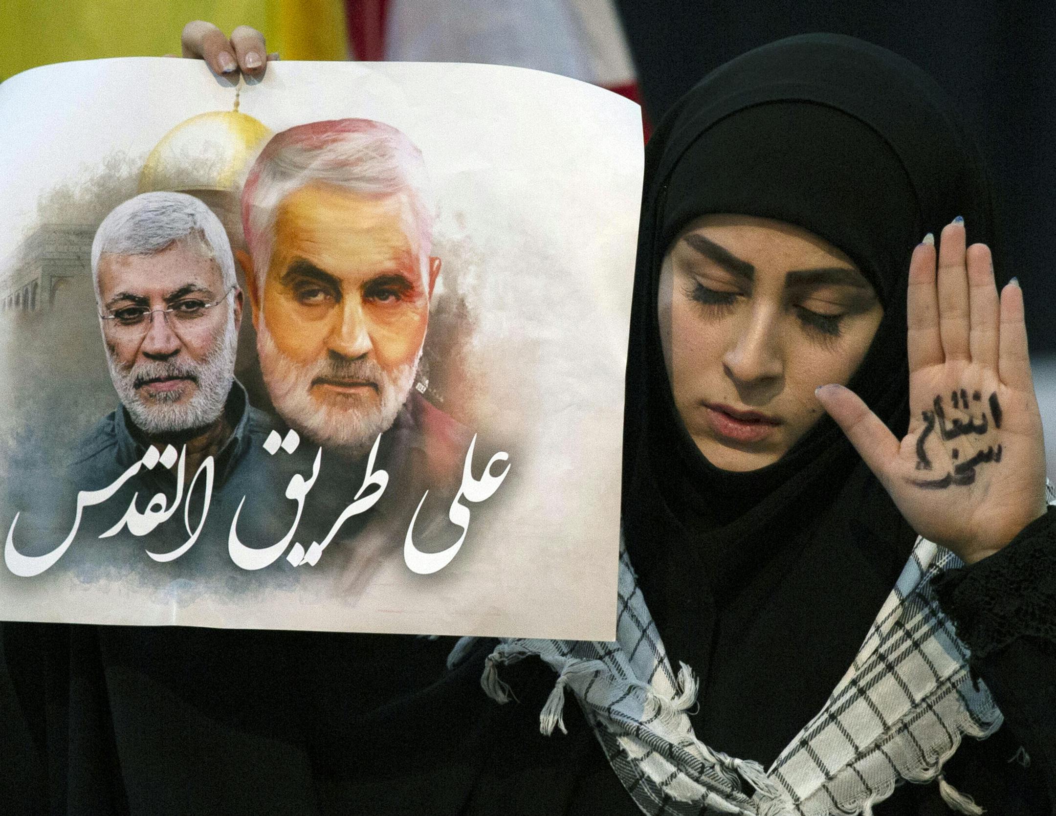 A supporter of Hezbollah leader Sayyed Hassan Nasrallah wears the words "powerful revenge" on her hand, ahead of the leader's televised speech in a southern suburb of Beirut, Lebanon, Sunday, Jan. 5, 2020 following the U.S. airstrike in Iraq that killed Iranian Revolutionary Guard Gen. Qassem Soleimani. The placard in her other hand depicts Soleimaini and Iraq's Popular Mobilization forces commander Abu Mahdi al-Muhandis, who was also killed in the strike. Arabic on placard reads: "On the road t