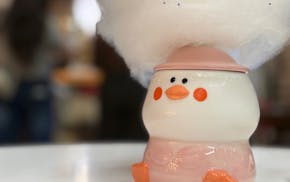 A squat ceramic duck mug with rosy cheeks and little feetsies has a cone hat and a swirl of sprinkle-dotted cotton candy coming out of his head. Sitti