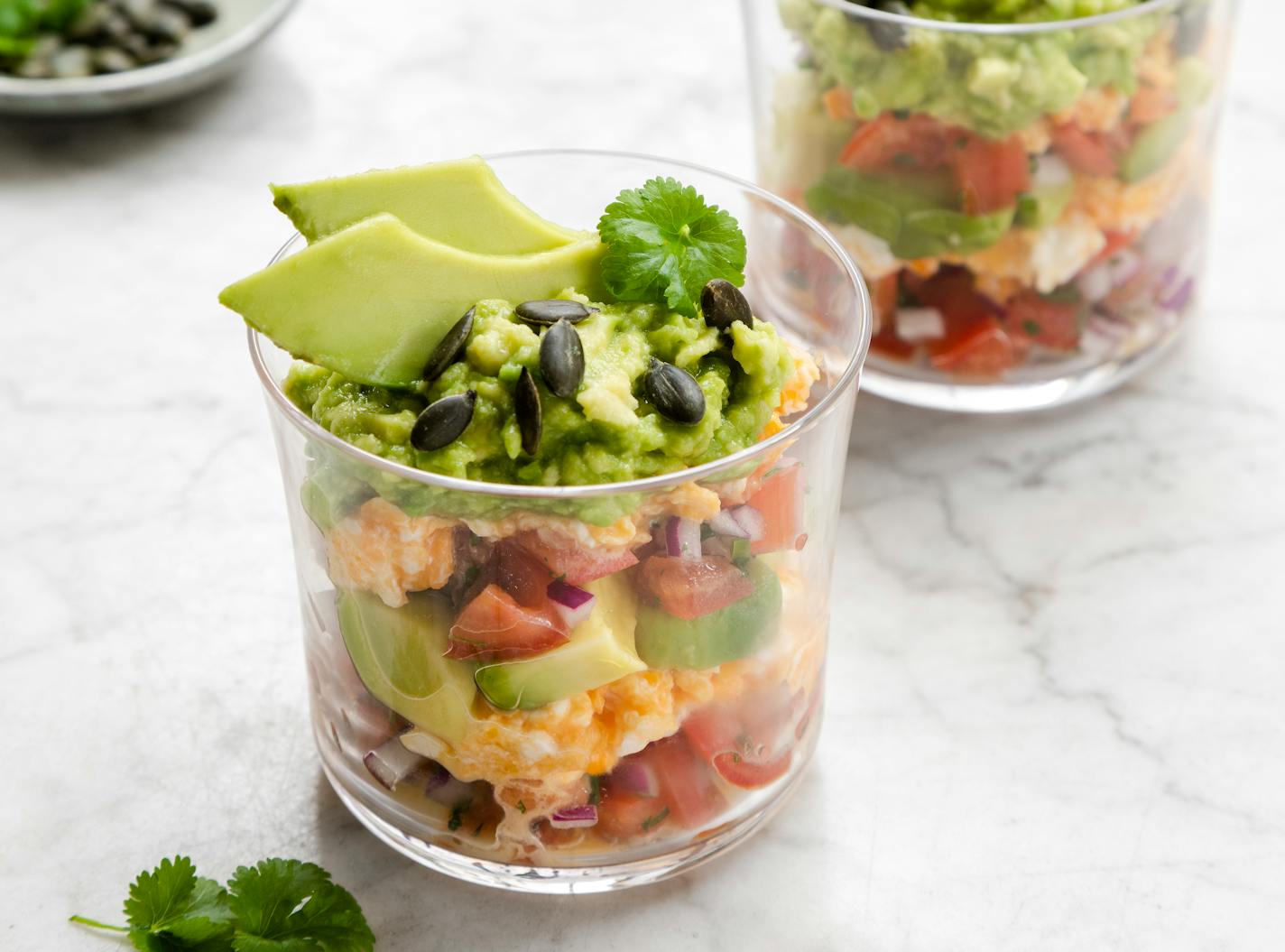 Scrambled eggs, avocados and tomatoes are layered in a drinking glass for a sundae affect.