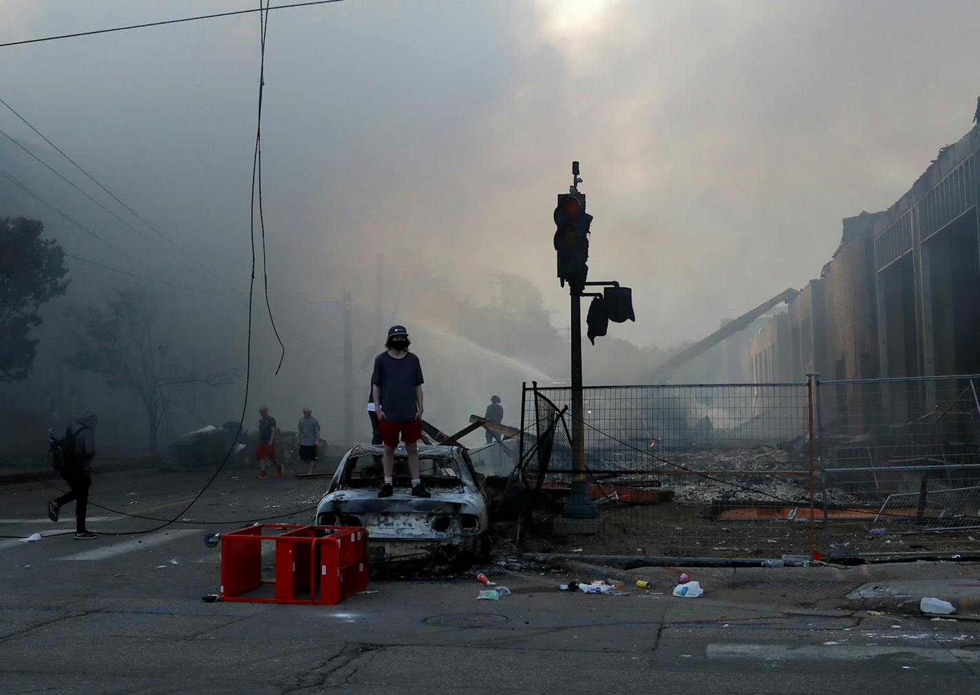 Dawn breaks after the second night of unrest in south Minneapolis, following the death Monday of unarmed George Floyd in Minneapolis Police custody. Here, a man stood on a burned out car near a burning building just off E. Lake Street Thursday, May 28, 2020, in Minneapolis, MN.] DAVID JOLES • david.joles@startribune.com aftermath of looting around lake street and Minnehaha, near 3rd precinct.