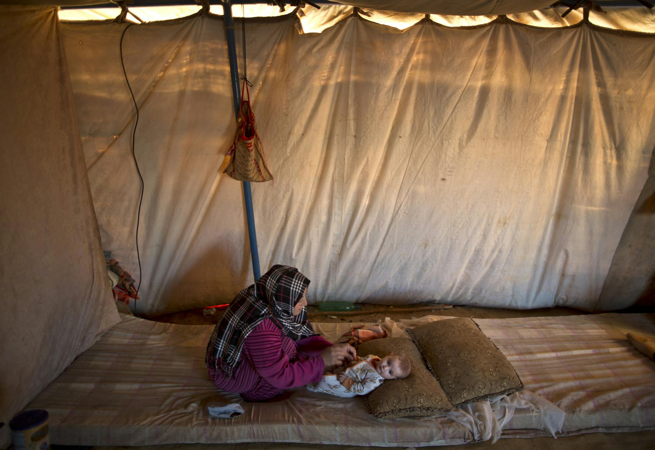 In this Tuesday, July 21, 2015 photo, Syrian refugee Naela Mohammed, 31, changes the clothes of her daughter Asmahan, 4 months, at their tent in an informal tented settlement near the Syrian border on the outskirts of Mafraq, Jordan. Naela worries about being able to nurse her child while she herself doesn’t have enough to eat. “It’s a sure thing my 4-month daughter will be paying the price,” Mohammed says. “She’s so tiny and weak.” (AP Photo/Muha