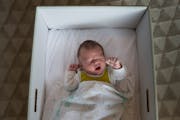 An infant in a Kela maternity package box, which is distributed — filled with bedding, infant clothing and other useful items — to all new mothers