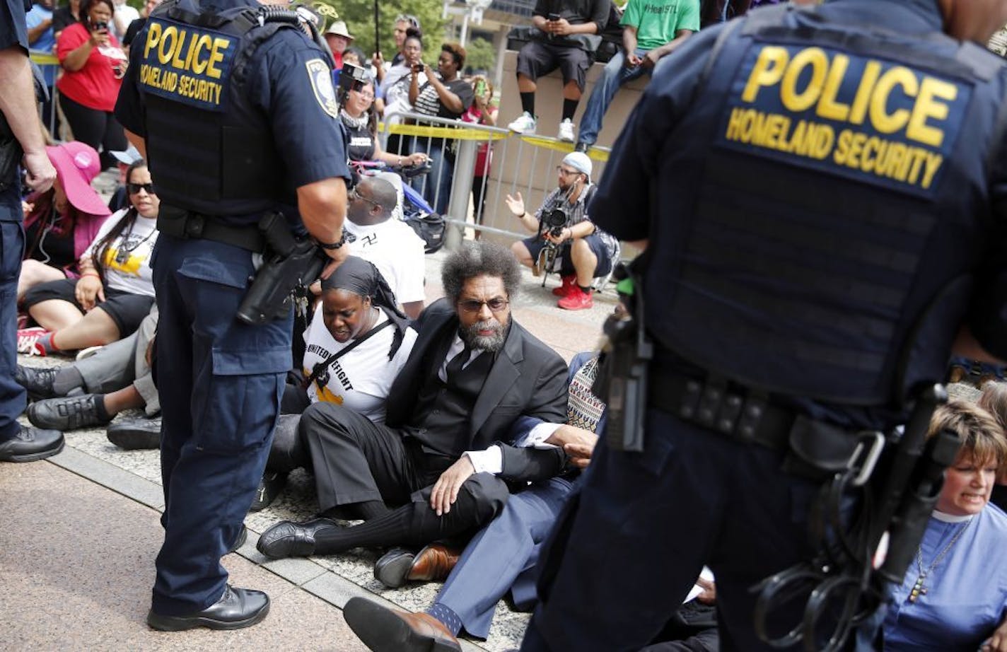 Cornel West, center, joins other protesters sitting on the steps of the Thomas F. Eagleton Federal Courthouse as members of the Federal Protective Service stand watch Monday, Aug. 10, 2015, in St. Louis. Protesters have been arrested after blocking the entrance to a St. Louis federal courthouse while calling for more aggressive U.S. government response to what they call racist law enforcement practices.