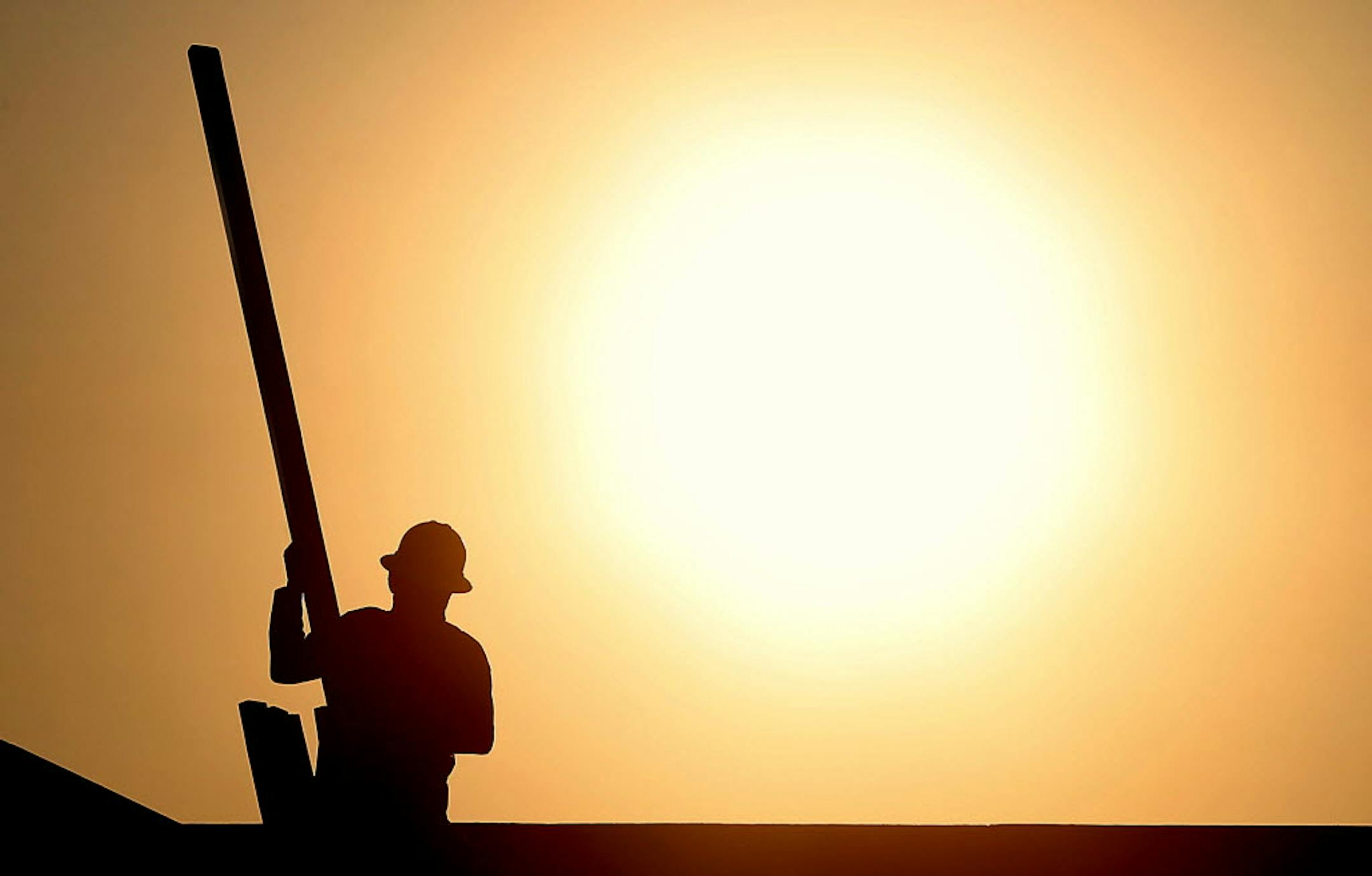 A construction worker is shown atop a roof at sunrise to beat daytime high temperatures Thursday in Queen Creek, Ariz.