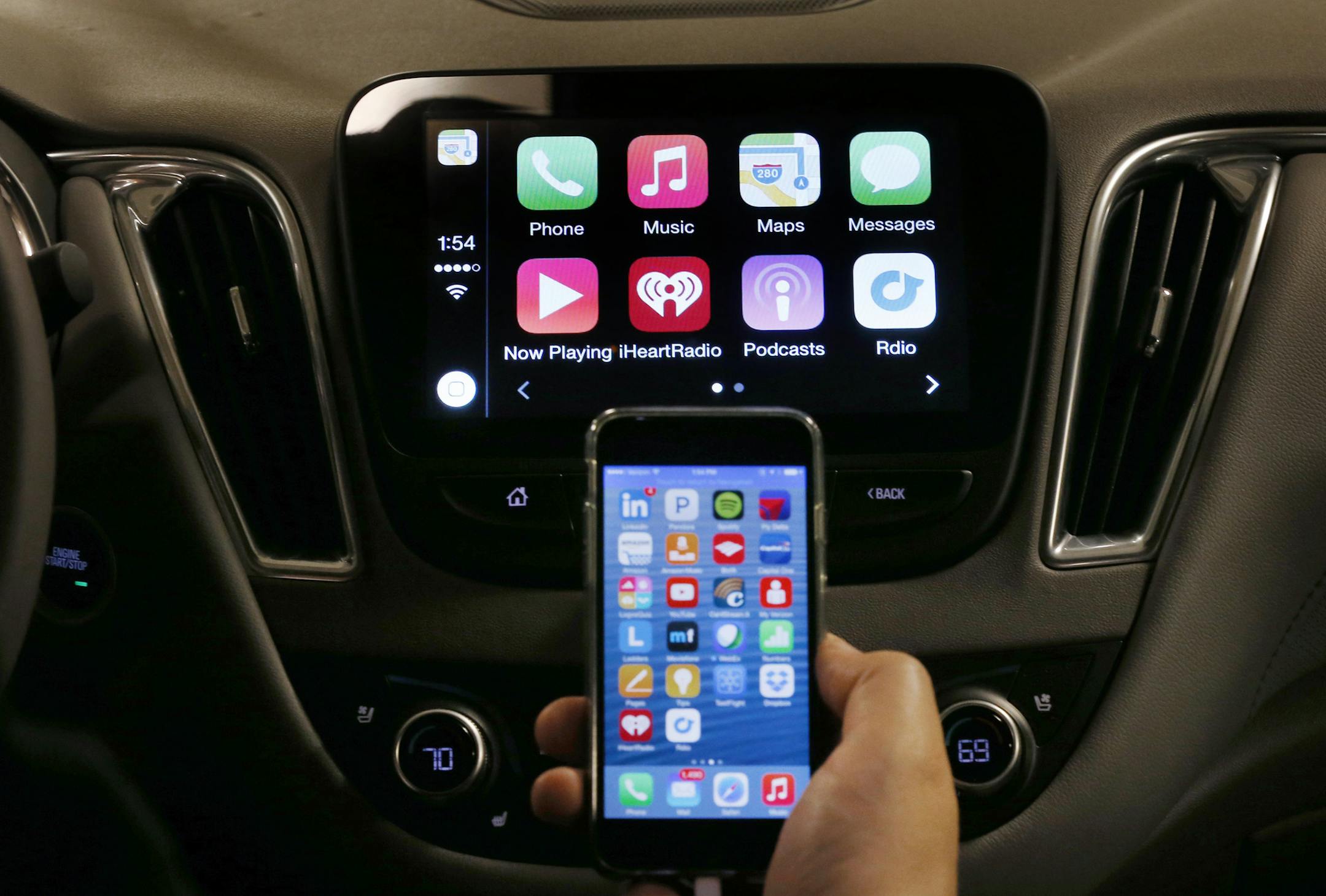 An iPhone is connected to a 2016 Chevrolet Malibu equipped with Apple CarPlay apps, displayed on the car's MyLink screen, top, during a demonstration in Detroit, Tuesday, May 26, 2015. Starting with Chevrolet this summer, many General Motors models will offer Apple&#xed;s CarPlay and Google&#xed;s Android Auto systems that link smart phones with in-car screens and electronics. (AP Photo/Paul Sancya) ORG XMIT: MIPS201