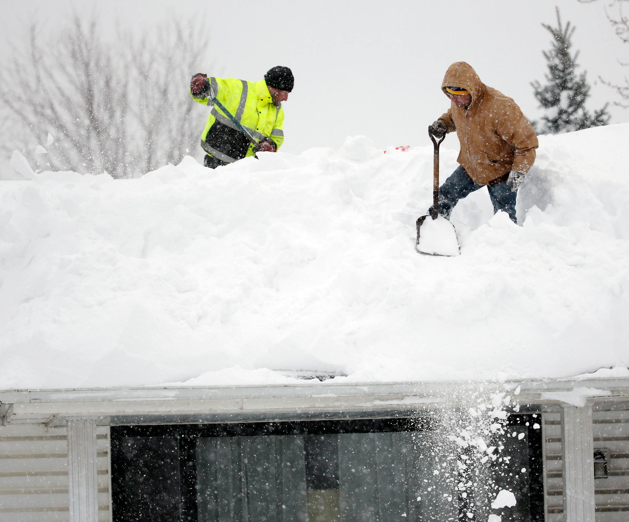 Mark Settlemyer, left, gets help clearing snow from the roof of his mother's house from Ken Wesley on Wednesday, Nov. 19, 2014, in Lancaster, N.Y. Lake-effect snow pummeled areas around Buffalo for a second straight day, leaving residents stuck in their homes as officials tried to clear massive snow mounds with another storm looming. (AP Photo/Mike Groll)