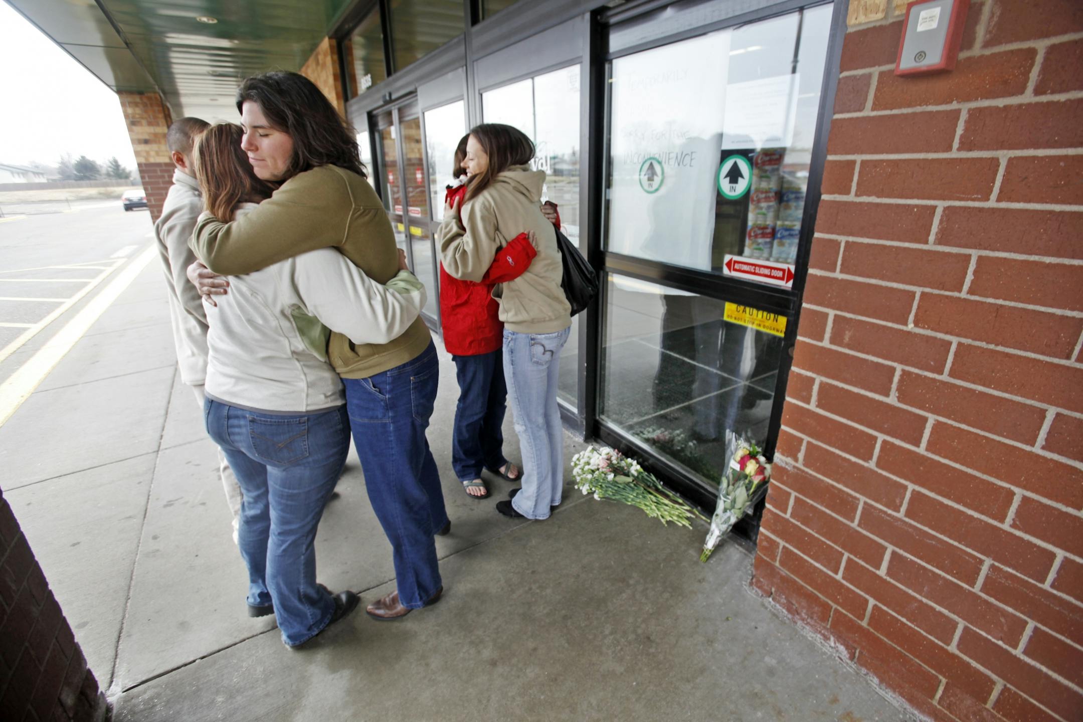 After leading church members in prayer, Rev. Rachel McIver Morey of Mosaic Church, front center, hugged Tanya Baity, front left, outside of the closed Festival Foods Saturday. McIver Morey, who heard about the incident via Twitter, said they came to the grocery store to help the community and store employees with healing. Two bouquets of flowers had been left outside the grocery store's doors.