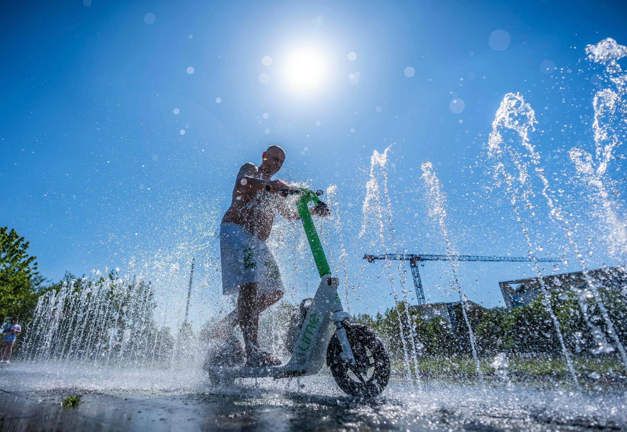 Tomas from Berlin rides his e-scooter through the water fontaine in front of the Chancellery in Berlin, Germany, Wednesday, July2, 2025.