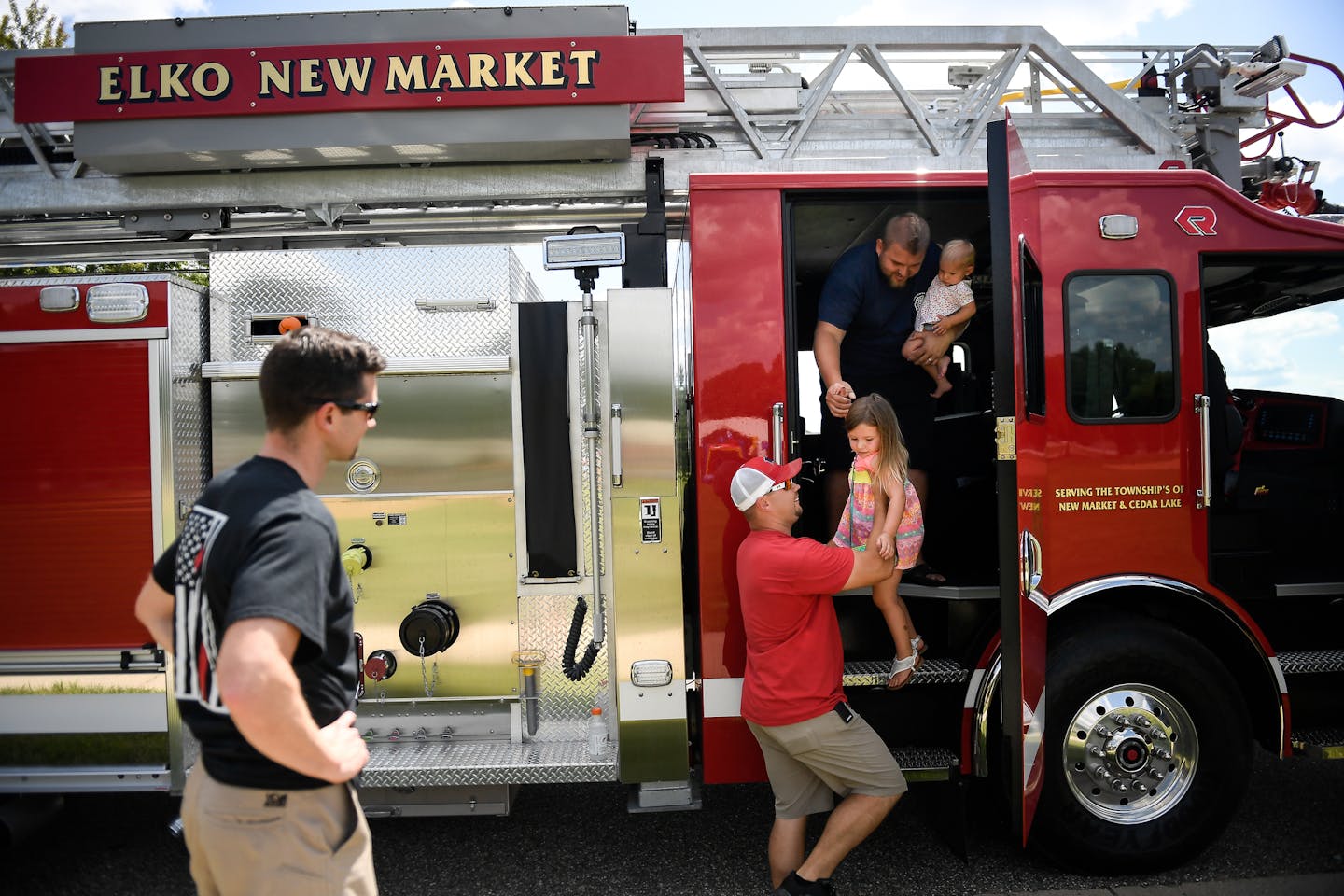 Elko New Market firefighter Jesse Stapp, left, watched as fellow firefighter Shawn Appleton, top right, passed his daughter Kennedy, 3, down to Josh Wichner as they attended Elko New Market's 10-year anniversary celebration of their city's merger in August. Appleton was also holding his younger daughter, Paisley, 1. ] AARON LAVINSKY &#xef; aaron.lavinsky@startribune.com It's been 10 years since Elko and New Market merged into the small affluent suburb of Elko New Market, yet residents seem to be