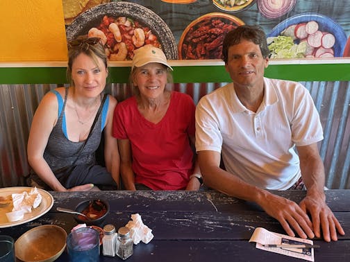 A woman and her parents are seated in a restaurant with a colorful backdrop.