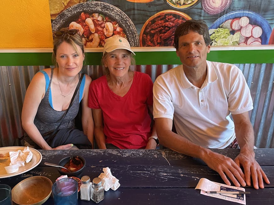 A woman and her parents are seated in a restaurant with a colorful backdrop.