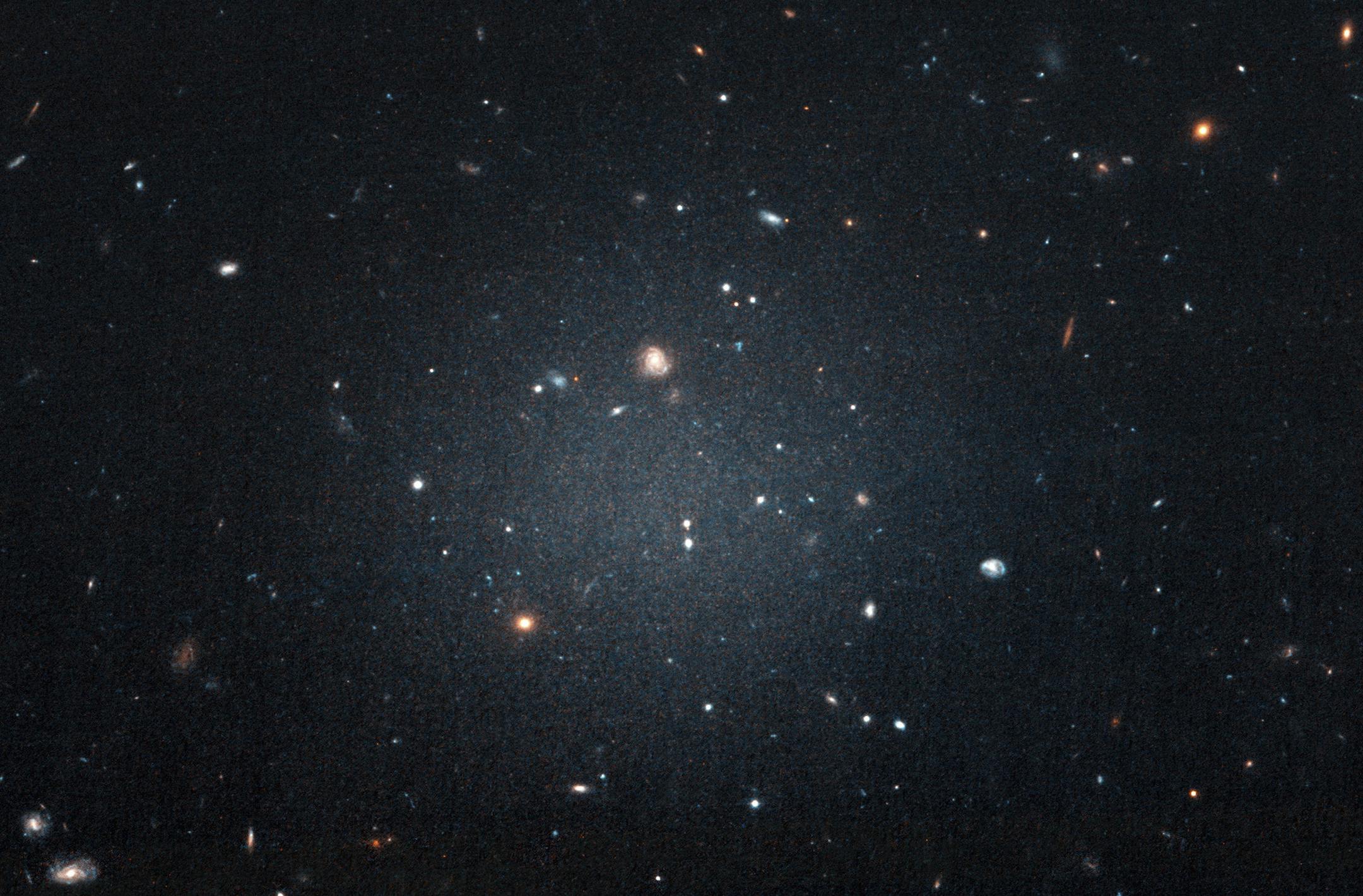 This Nov. 16, 2017 image made with the Hubble Space Telescope shows the diffuse galaxy NGC 1052-DF2, lighter area in center. Several other galaxies can be seen through it. The unusual galaxy&#x2019;s stars are speeding around with no apparent influence from dark matter, according to a study published on Wednesday, March 28, 2018 in the journal Nature. (P van Dokkum/NASA/ESA via AP)