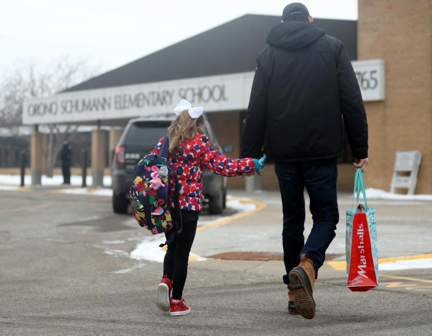 A parent walks his child to Orono Schumann Elementary School as a police officer stands nearby as students arrive for the day Thursday, Feb. 22, 2018, a day after a threat was posted, causing Orono schools to go on lockdown. A student was arrested at the high school Wednesday after a threat of gun violence.