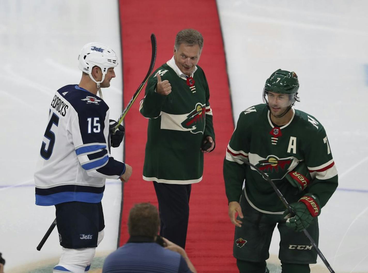 Finland President Sauli Niinisto gave a thumbs-up after he took part in a ceremonial dropping of the puck with Winnipeg Jets center Matt Hendricks (15) and Minnesota Wild center Matt Cullen (7) before an NHL hockey preseason game Thursday, Sept. 21, 2017, in Minneapolis.