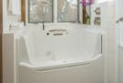 The Kohler Rising Wall Bath, with a chair height seat, fits in an alcove in this remodeled master bathroom.