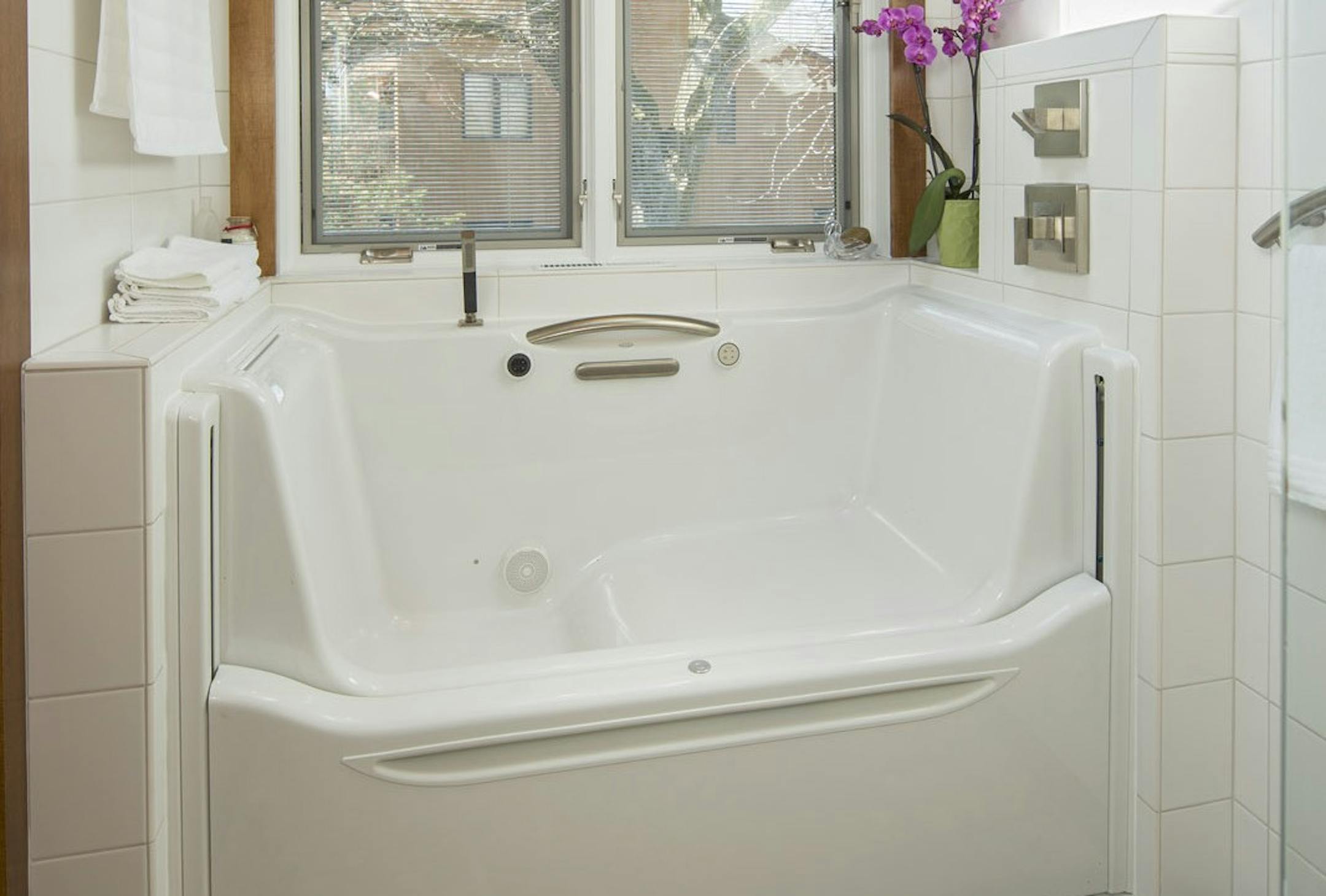 The Kohler Rising Wall Bath, with a chair height seat, fits in an alcove in this remodeled master bathroom.