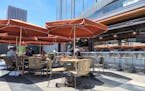 A patio with a bar and tables with rust-colored umbrellas, surrounded by glass buildings