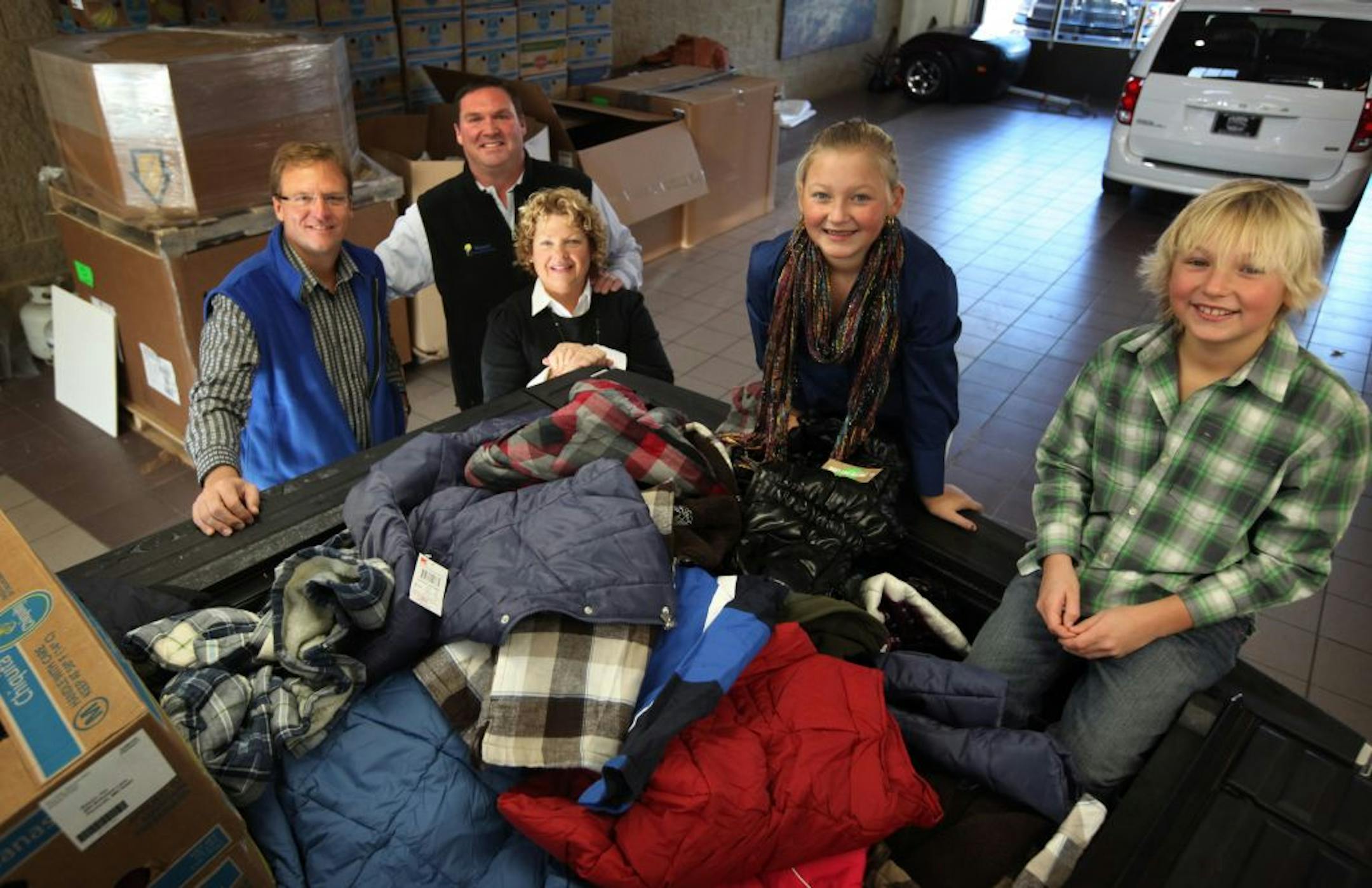 Eric Wenzel started a winter coat drive last year with two drop boxes and a simple idea to pay back a community that supported him during his fight with cancer. This year the effort has grown so big that Coats of Kindness had more than a dozen drop sites in the metro area. Here, (L TO R) Rom Leonard of Fury Motors, Eric Wenzel with his wife Karen and children Emma, 11, and Jake, 10, with the boxes of coats, hats and scarves that have been donated already this year.