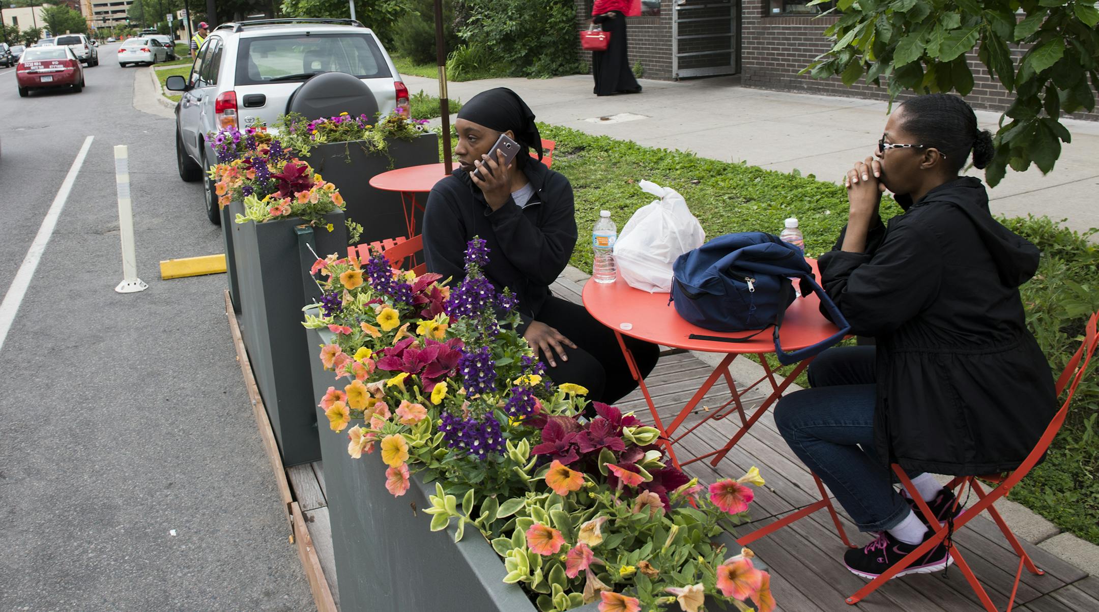 Shanay Ponder, left, answers a call while she sits with her mother, Inez Howard, at the new parklet seating outside of Twin Cities Coffee and Deli on Chicago Ave. on Wednesday. "This is the first time I've seen it," said Ponder of the new seating. "I love it." ] Isaac Hale ï isaac.hale@startribune.com The city is expanding its Parklet program to include "street cafes", pop-up spaces to eat in curbside parking spots outside restaurants.