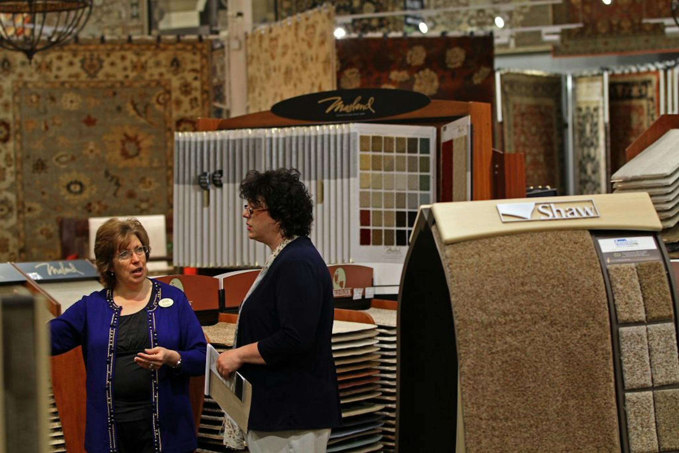 (left to right) Flooring Specialist Peggy Rock trained Flooring Specialist Rebecca Mezera on the vast selection at the new Hom Furniture floor and carpeting sections at the Plymouth store on 4/5/12. Despite a slow economic recovery, retailers see small but unmistakable signs of life in the sluggish home improvement market. It may not be the boom years but retailers are expanding into new categories and investing in new stores. HOM Furniture recently debuted its new floor and carpeting sections.