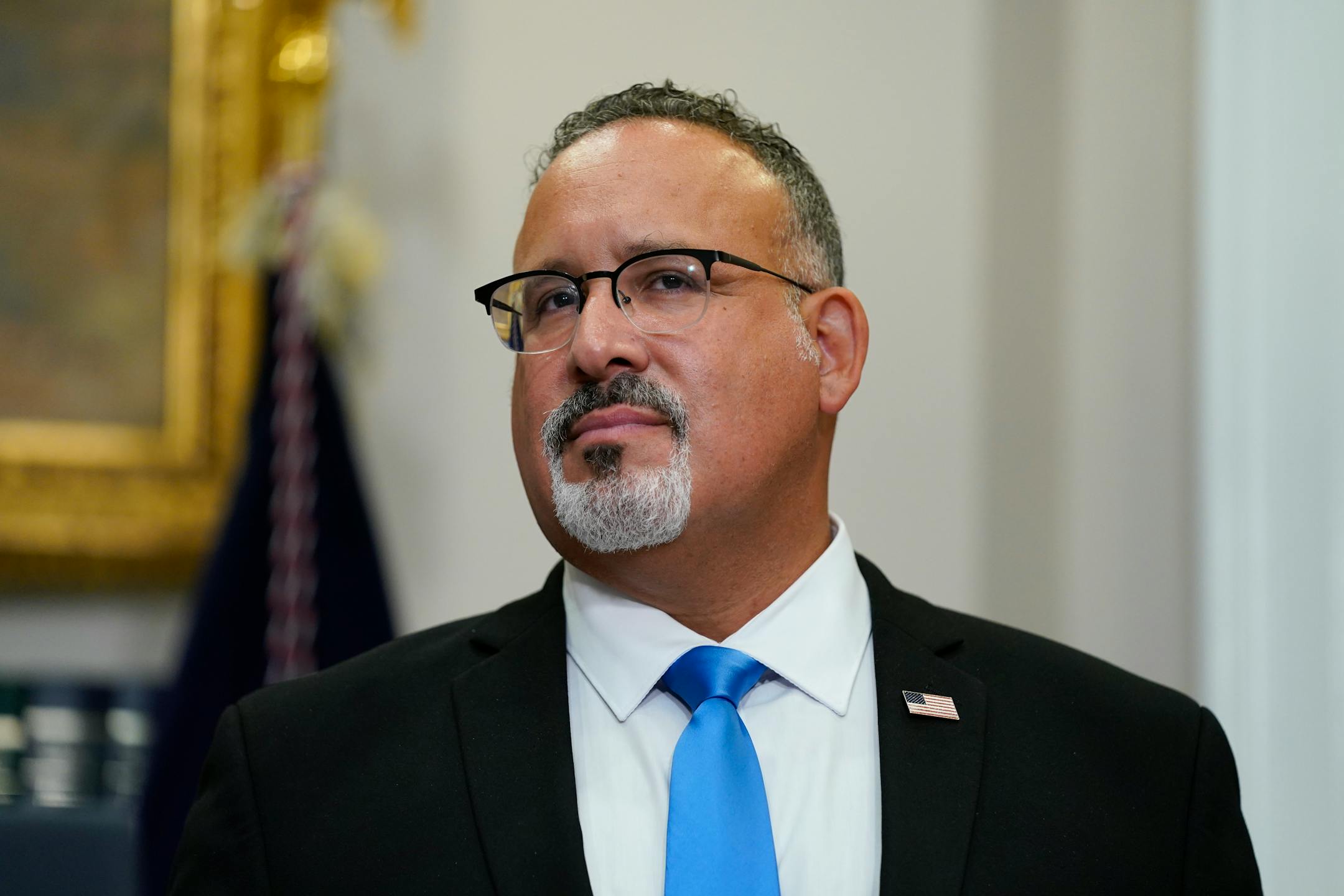 Education Secretary Miguel Cardona wearing a suit and blue tie.