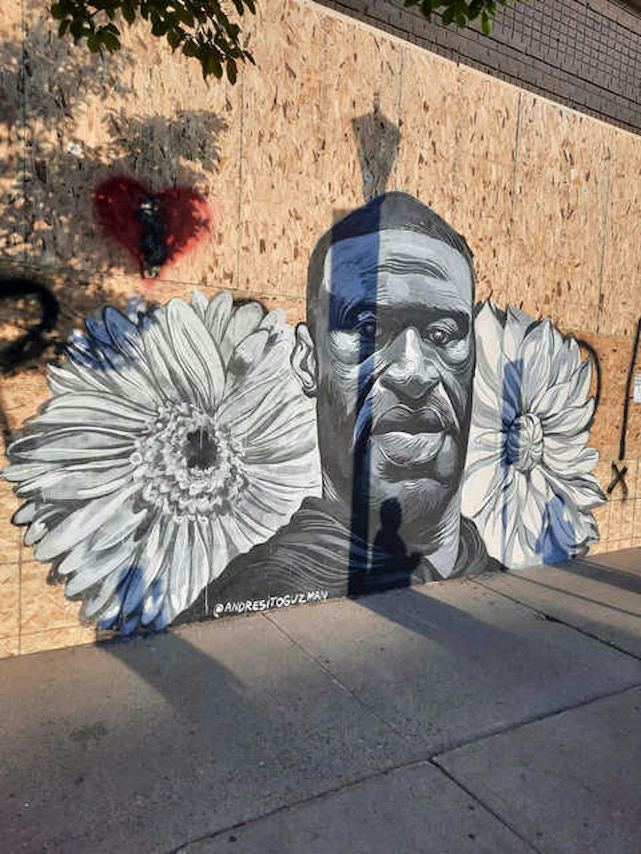 Artist Andres Guzman painted a gray, black and white-colored version of George Floyd surrounded by flowers on the boarded-up windows of hip-hop retailer Fifth Element, located at 2411 Hennepin Ave.