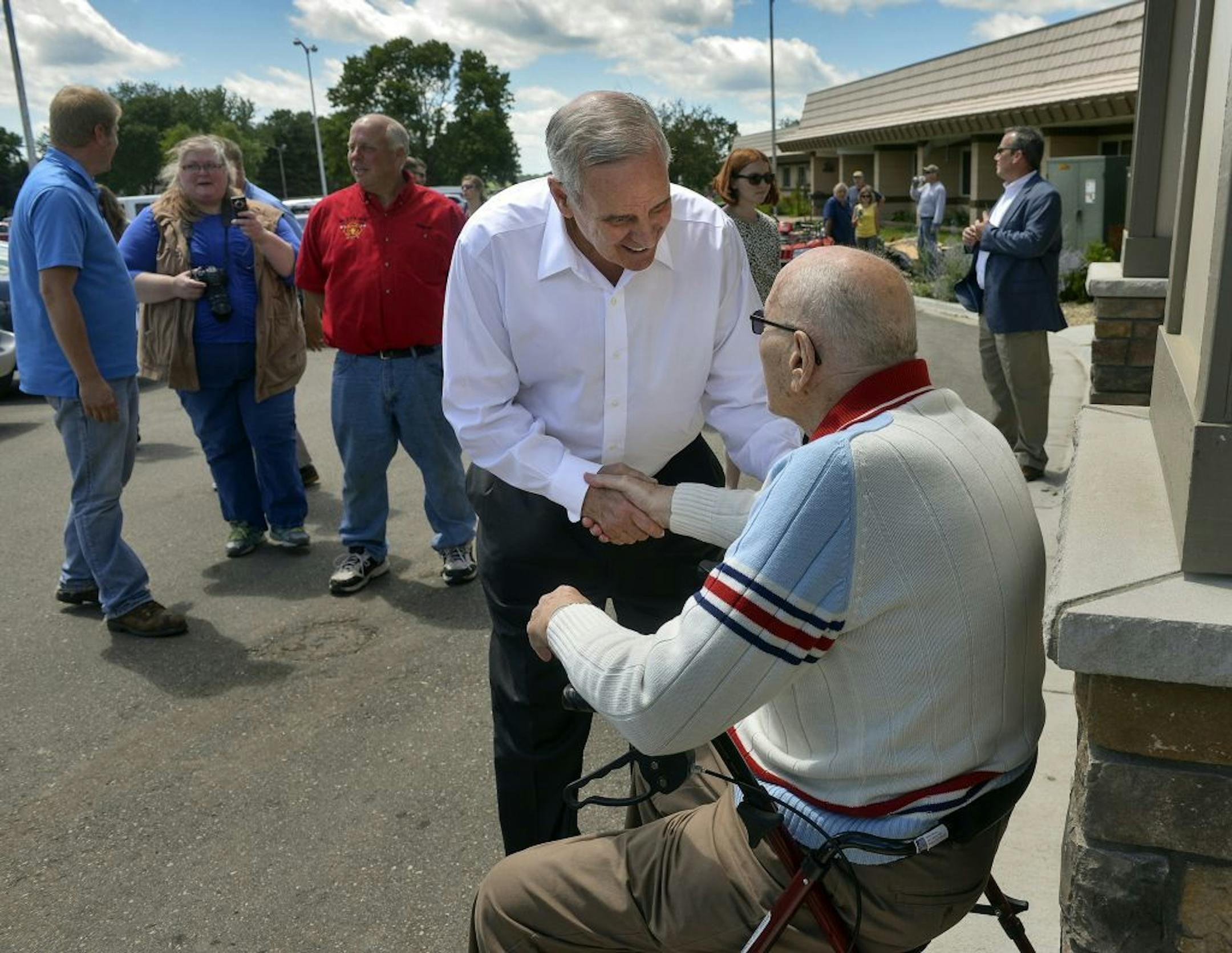 Minnesota Gov. Mark Dayton talks with Hilltop Health Care Center of Watkins resident Harold Sietsema outside the center during visit of the storm damaged town of Watkins, Minn., Wednesday, July 13, 2016.
