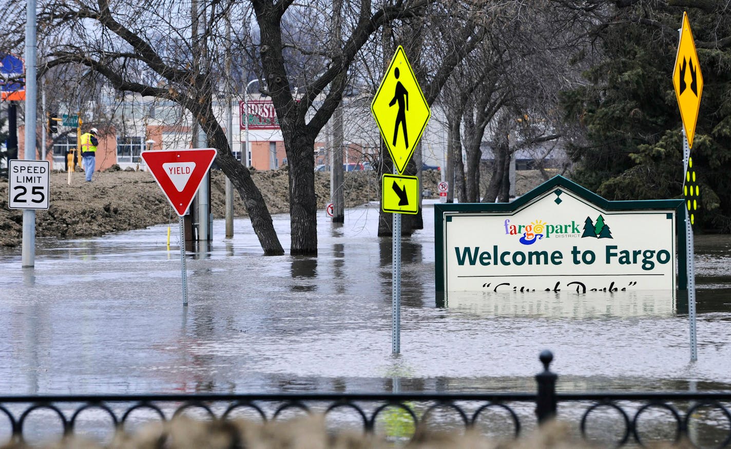 FILE - In this April 8, 2011 file photo, a welcome sign for Fargo, N.D., sits in the rising floodwaters of the Red River as a flood engineer for the U.S. Army Corps of Engineers, at left, inspects the levee protecting the downtown area.