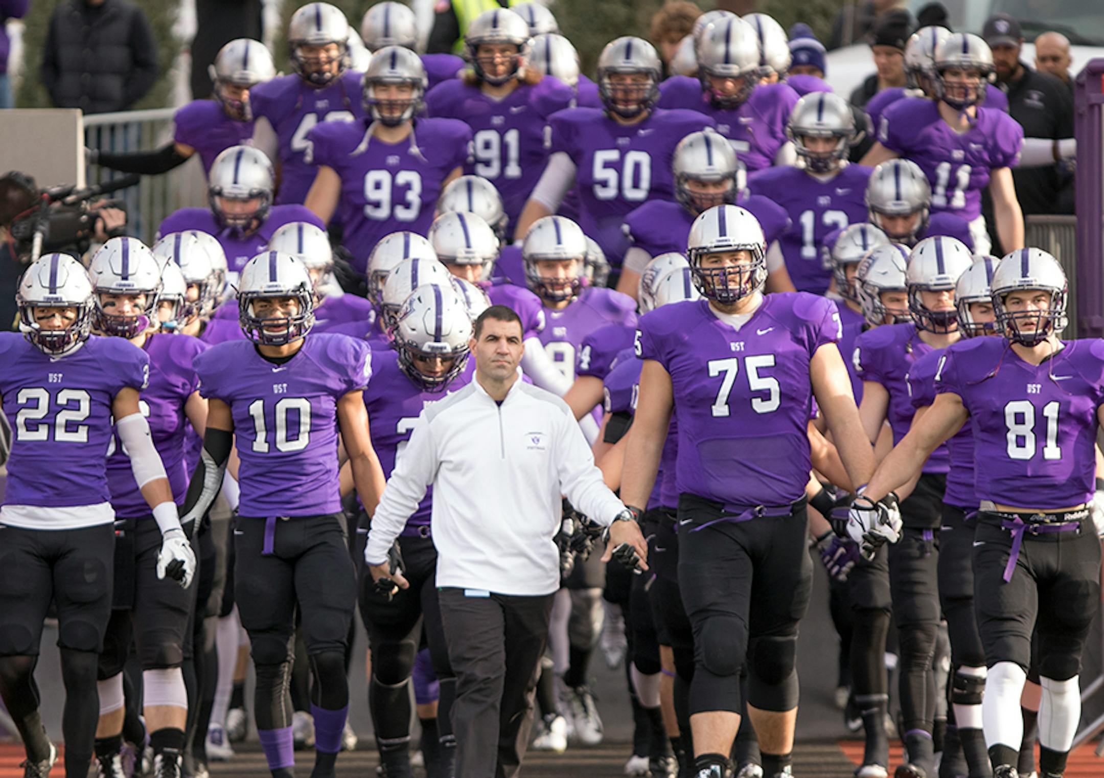 The St. Thomas football team enters the field before the game led by head coach Glenn Caruso, offensive lineman David Simmet (75), tight end Charlie Dowdle (81), cornerback Mozus Ikuenobe (10), and defensive back Jordan Young (22) as the University of St. Thomas Tommies hosted the Wabash College Little Giants on December 5, 2015.