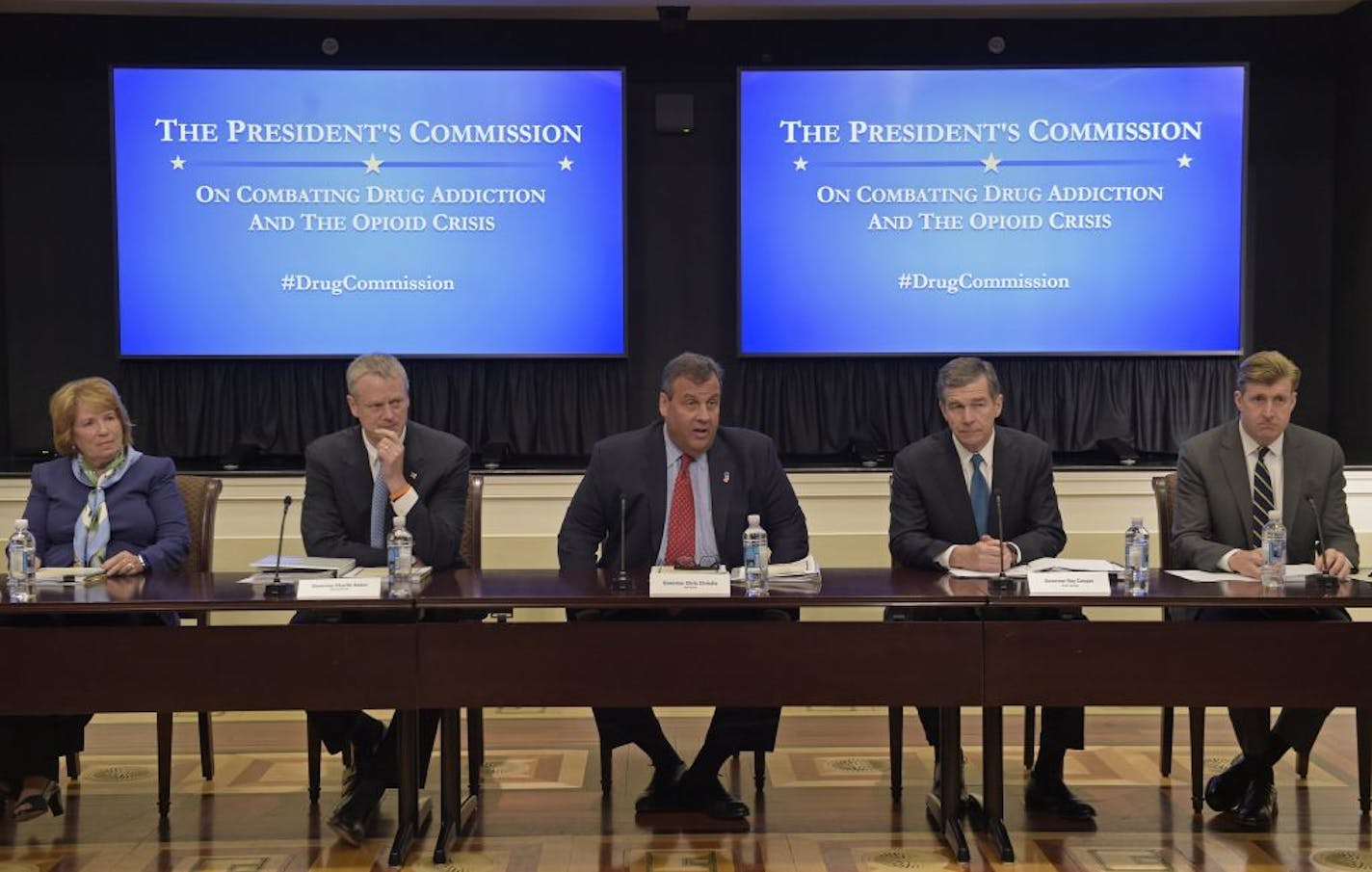 New Jersey Gov. Chris Christie, center, chairman of the President's Commission on Combating Drug Addiction and the Opioid Crisis, peaks at the beginning of the first meeting of the commission on combating drug addiction and the opioid crisis, Friday, June 16, 2017, in the Eisenhower Executive Office Building at the White House complex in Washington. From left are , Dr. Bertha K. Madras, a Harvard Medical School professor who specializes in addiction biology, Massachusetts Gov. Charlie Baker, Chr