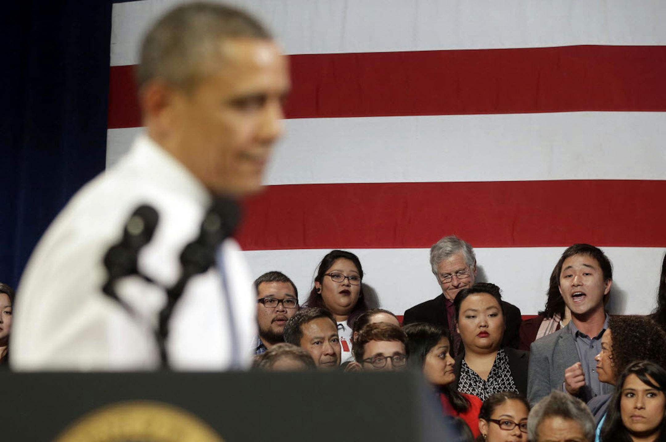 In this Nov. 25, 2013, photo, President Barack Obama, left, stops his speech and turns around in response to an unidentified man, right, who heckled him about anti-deportation policies, at the Betty Ann Ong Chinese Recreation Center in San Francisco.