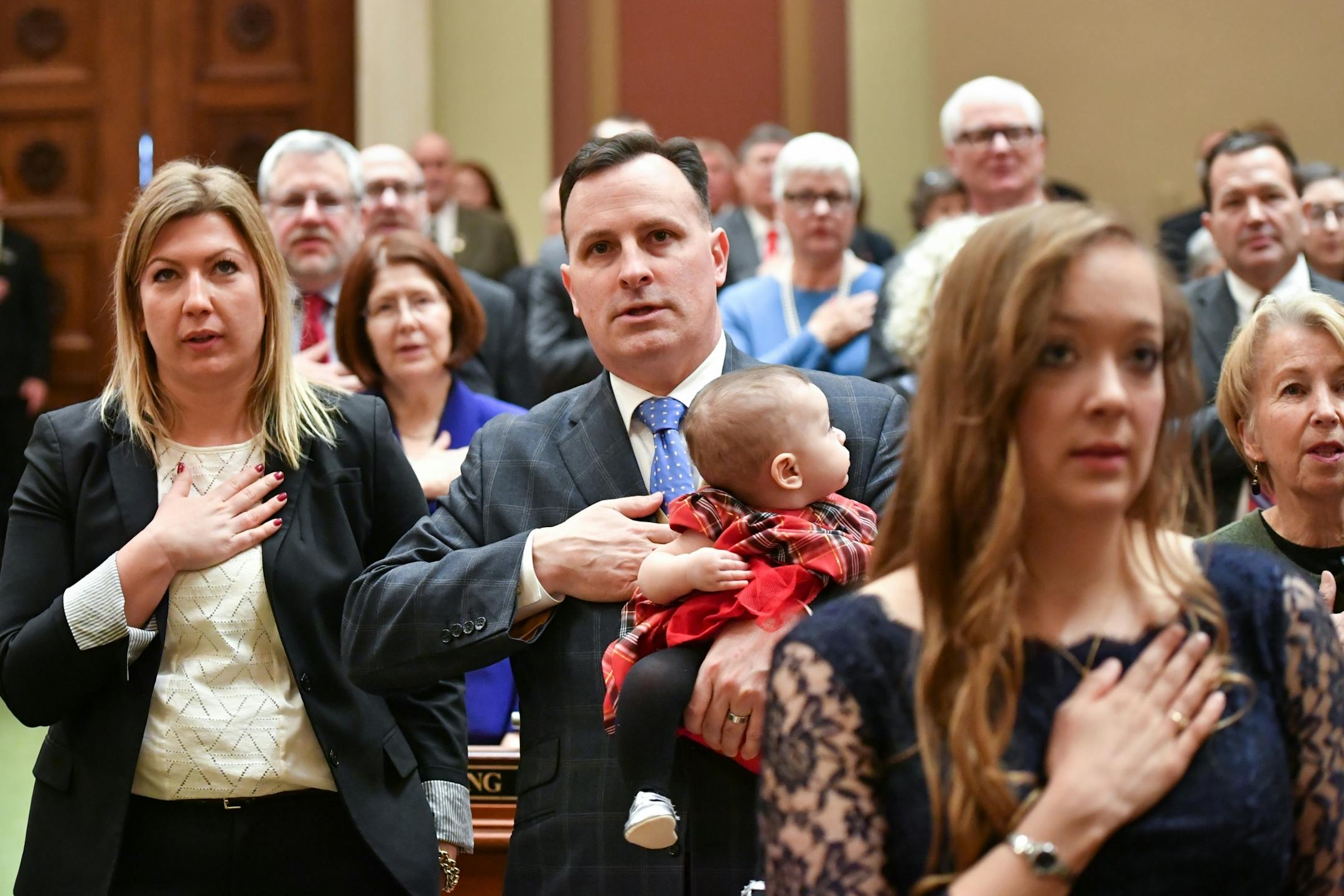 Rep John Lesch, DFL-St. Paul, held his daughter as he held his hand over his heart for the Pledge of Allegiance.