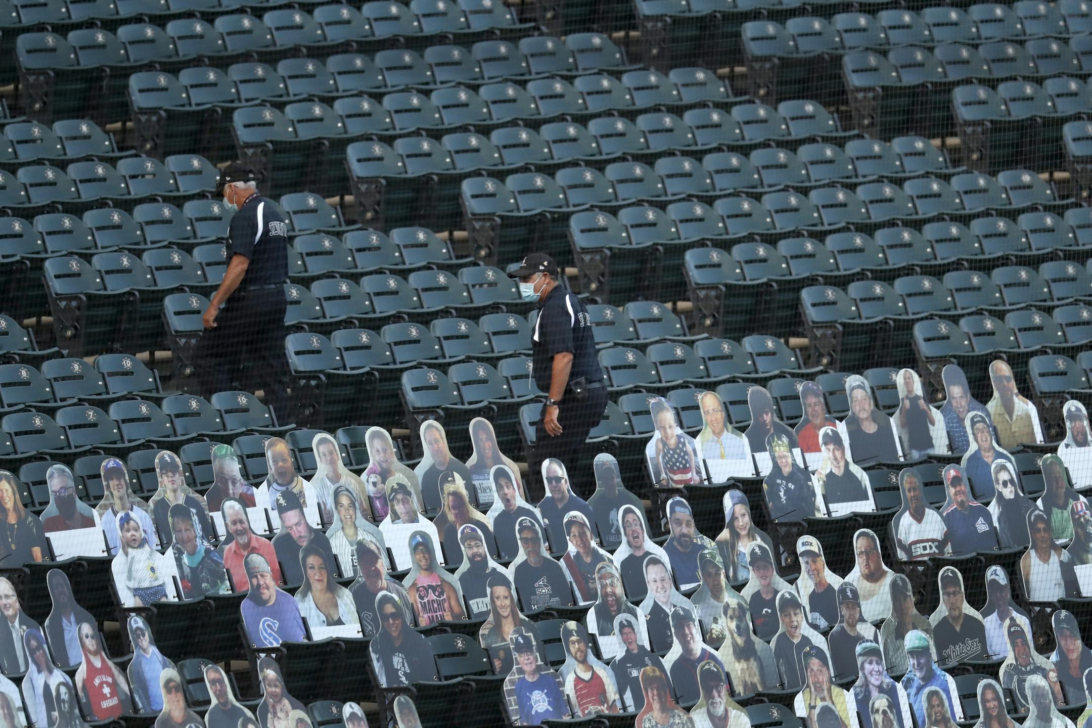 Security personnel walk through the seats and past cardboard cutouts of fane before an opening days baseball game between the Chicago White Sox and the Minnesota Twins, Friday, July 24, 2020, in Chicago.