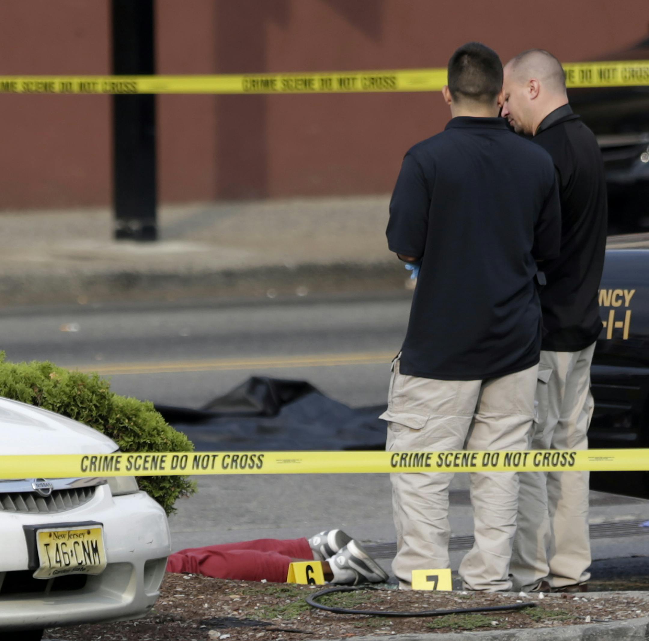 A person lays on the ground near evidence markers as officials investigate the scene where a Jersey City Police Department officer was shot and killed while responding to a call at a 24-hour pharmacy, Sunday, July 13, 2014, in Jersey City, N.J. Officer Melvin Santiago was shot in the head while still in his police vehicle as he and his partner responded to an armed robbery call at about 4.a.m., Jersey City Mayor Steven Fulop said in a statement. Fulop said officers responding to the robbery call
