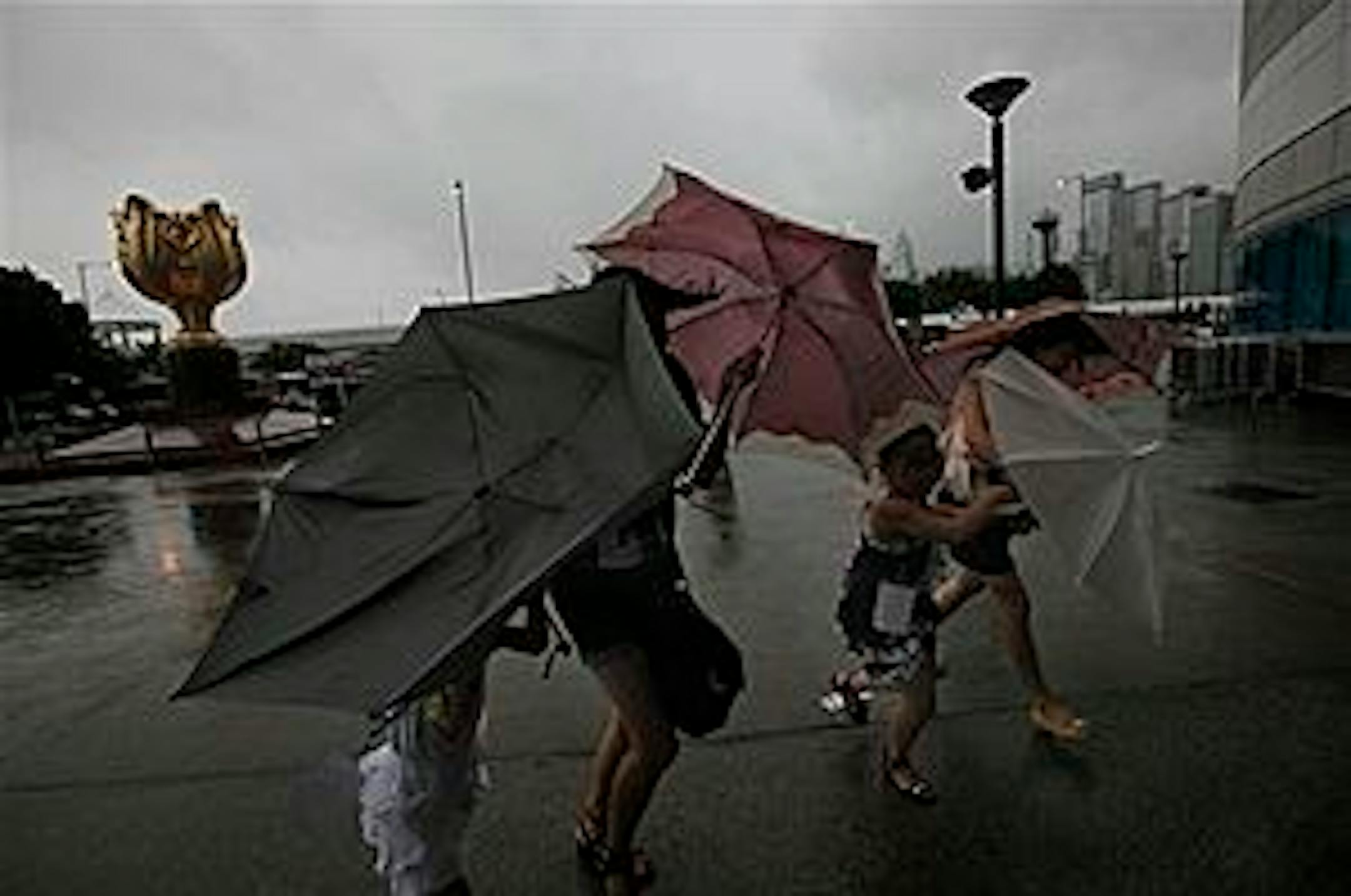People hold umbrellas as they walk through a strong wind near a ferry pier in Hong Kong Wednesday, July 21, 2010. Tropical Storm Chanthu was estimated to be about 410 kilometers (255 miles) south of Hong Kong. The outer rain bands of Chanthu are affecting Hong Kong as it continues to move closer, winds are also expected to strengthen overnight, the Hong Kong Observatory said. (AP Photo/Vincent Yu)