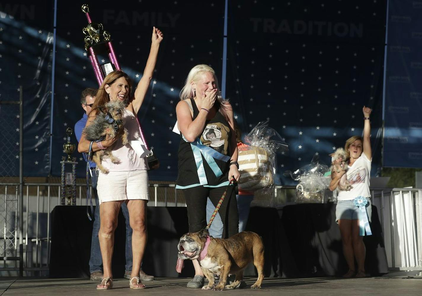 Megan Brainard, center, reacts after her dog Zsa Zsa, an English Bulldog, bottom, is announced the winner of the World's Ugliest Dog Contest at the Sonoma-Marin Fair in Petaluma, Calif., Saturday, June 23, 2018. Also pictured at left is Yvonne Morones, holding her dog Scamp, who placed second, and Linda Elmquist, holding her dog Josie, who finished third.