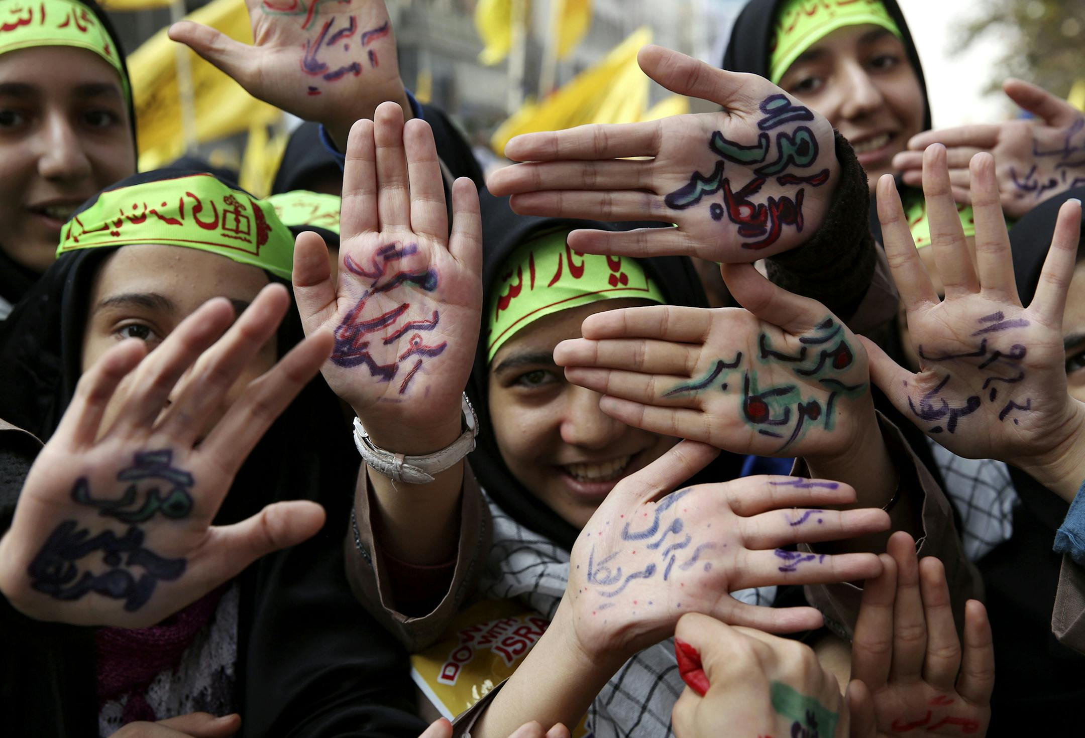 Iranian school girls raise their palms with Persian that reads, "death to America," during an anti-American rally in Tehran, Iran, Monday, Nov. 4, 2013. Tens of thousands of demonstrators packed the streets Monday outside the former U.S. Embassy in Tehran in the biggest anti-American rally in years, a show of support for hard-line opponents of President Hassan Rouhani's historic outreach to Washington. (AP Photo/Ebrahim Noroozi) ORG XMIT: MIN2013111211493241