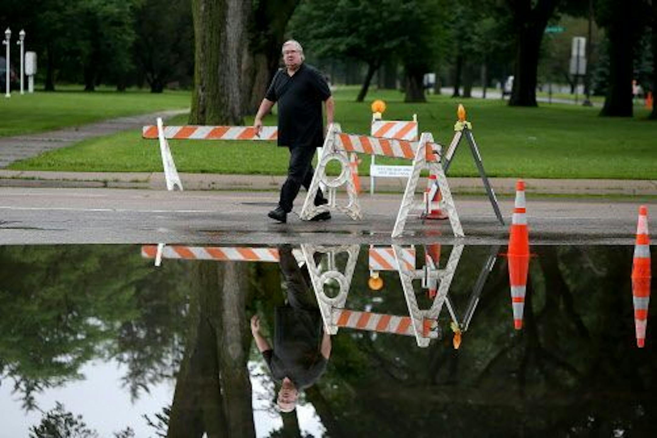 A pedestrian moved barriers for traffic to get through some dry stretches along flooded areas near Cedar Avenue and Minnehaha Parkway, Friday, June 20, 2014 in Minneapolis.