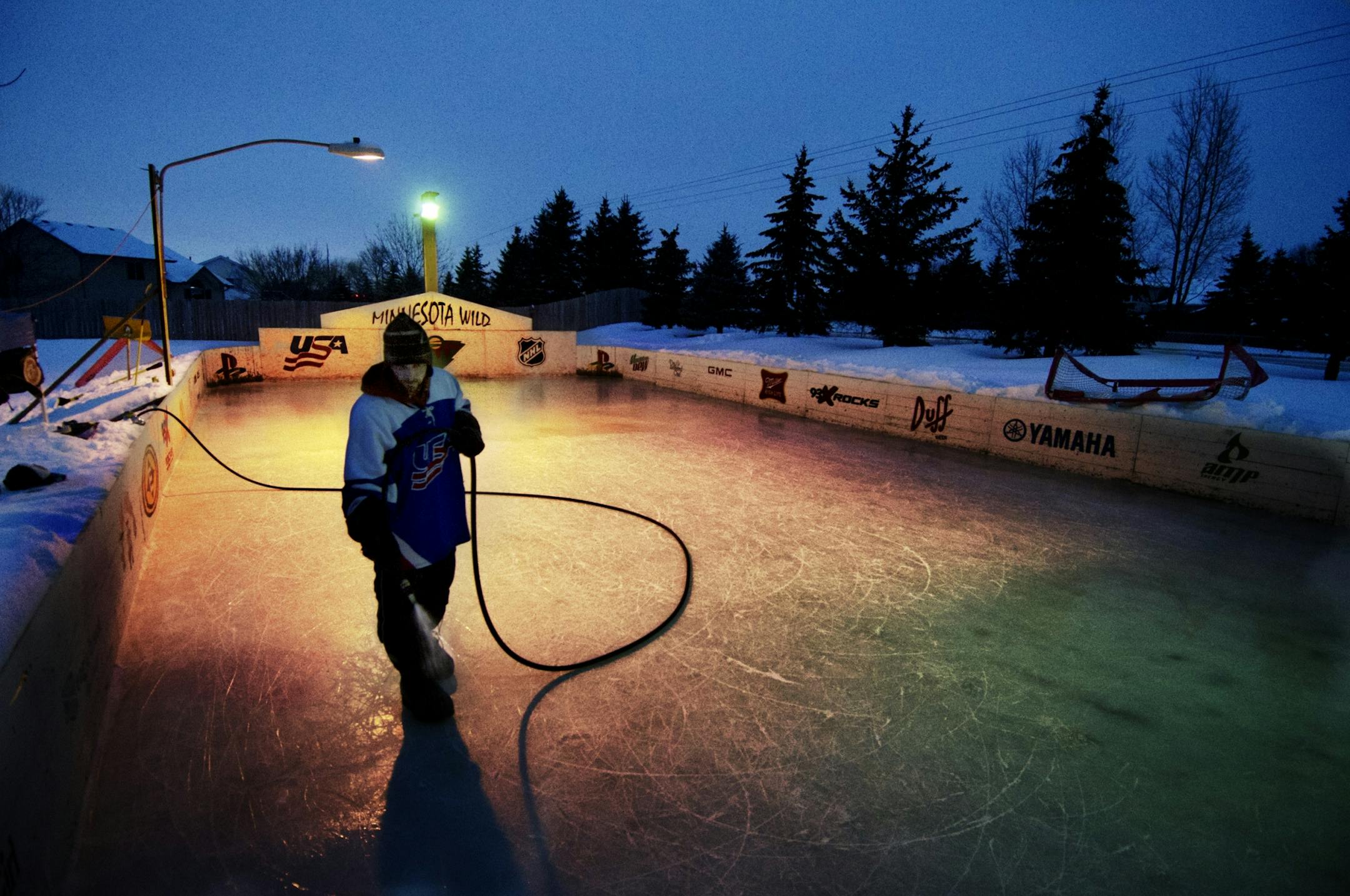 Dave Rouf uses a garden hose to add a fresh layer of water, soon to become ice, to his backyard rink.